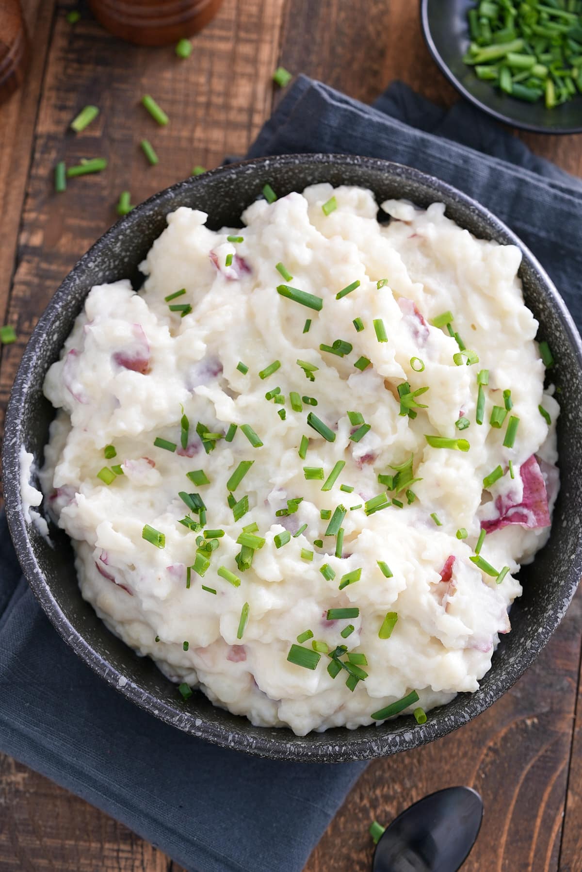 A bowl of mashed red skinned potatoes garnished with finely chopped chives.