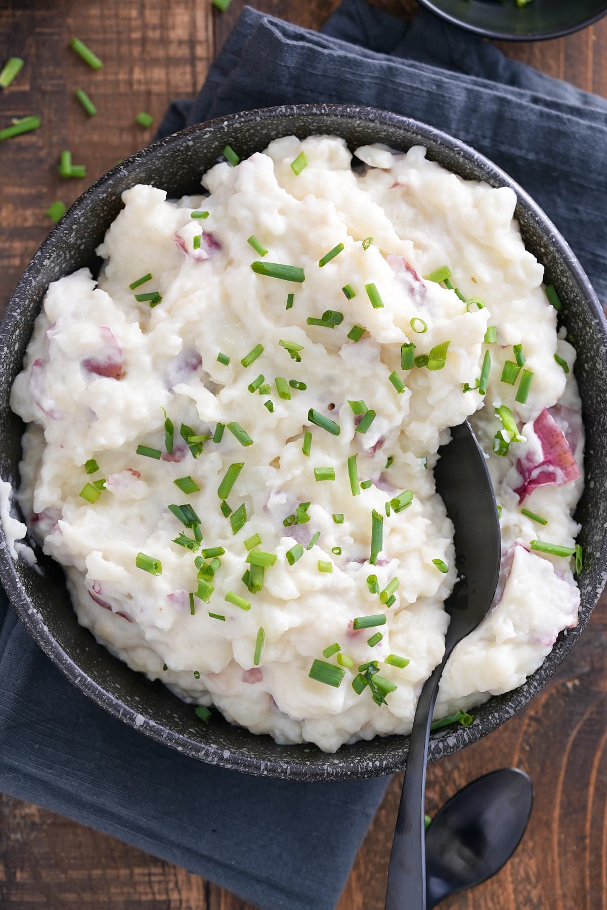 A bowl of mashed red skinned potatoes garnished with finely chopped chives.
