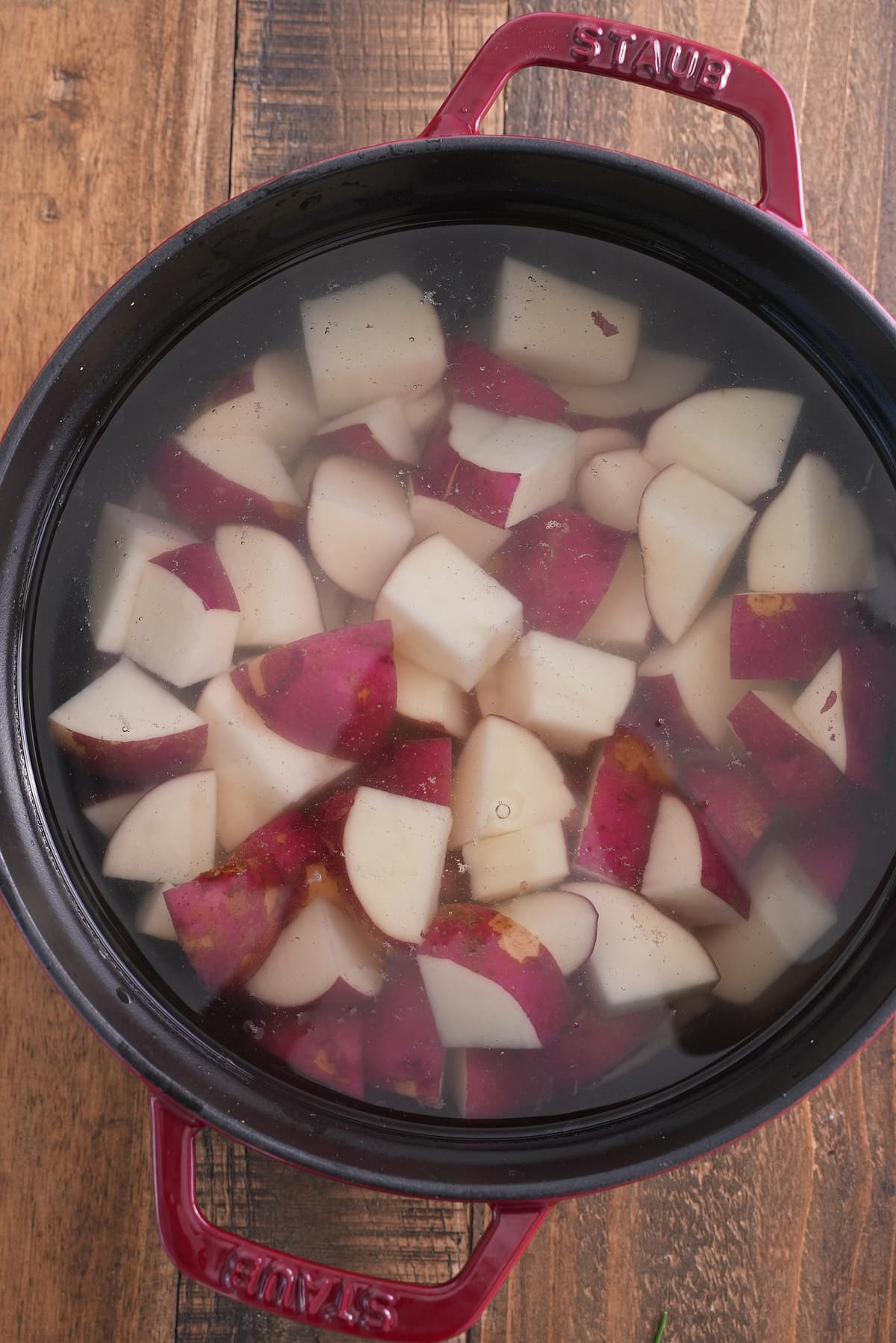 A Dutch oven filled with chopped red skinned potatoes, covered in water.