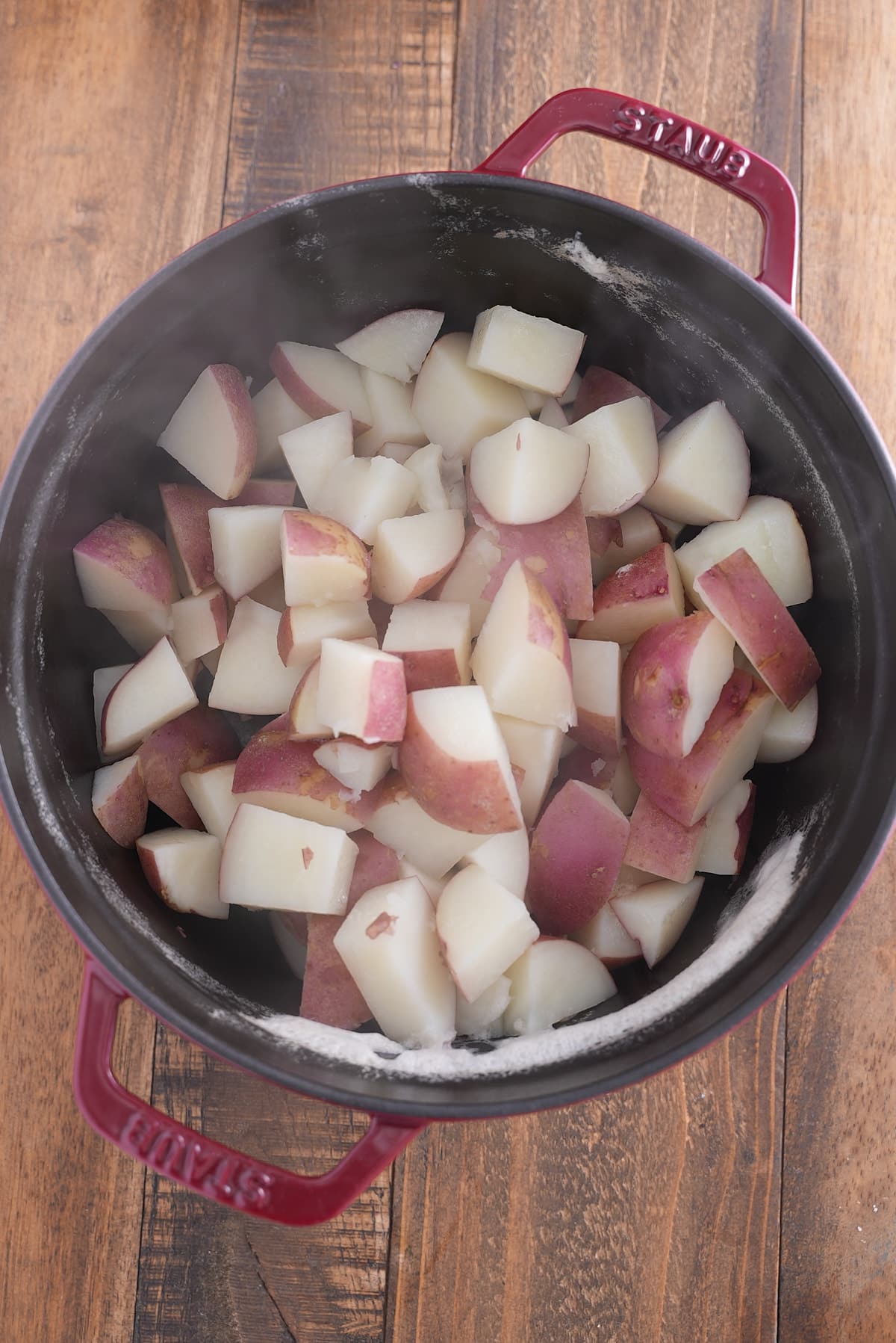 A Dutch oven filled with cooked and drained red skinned potatoes.