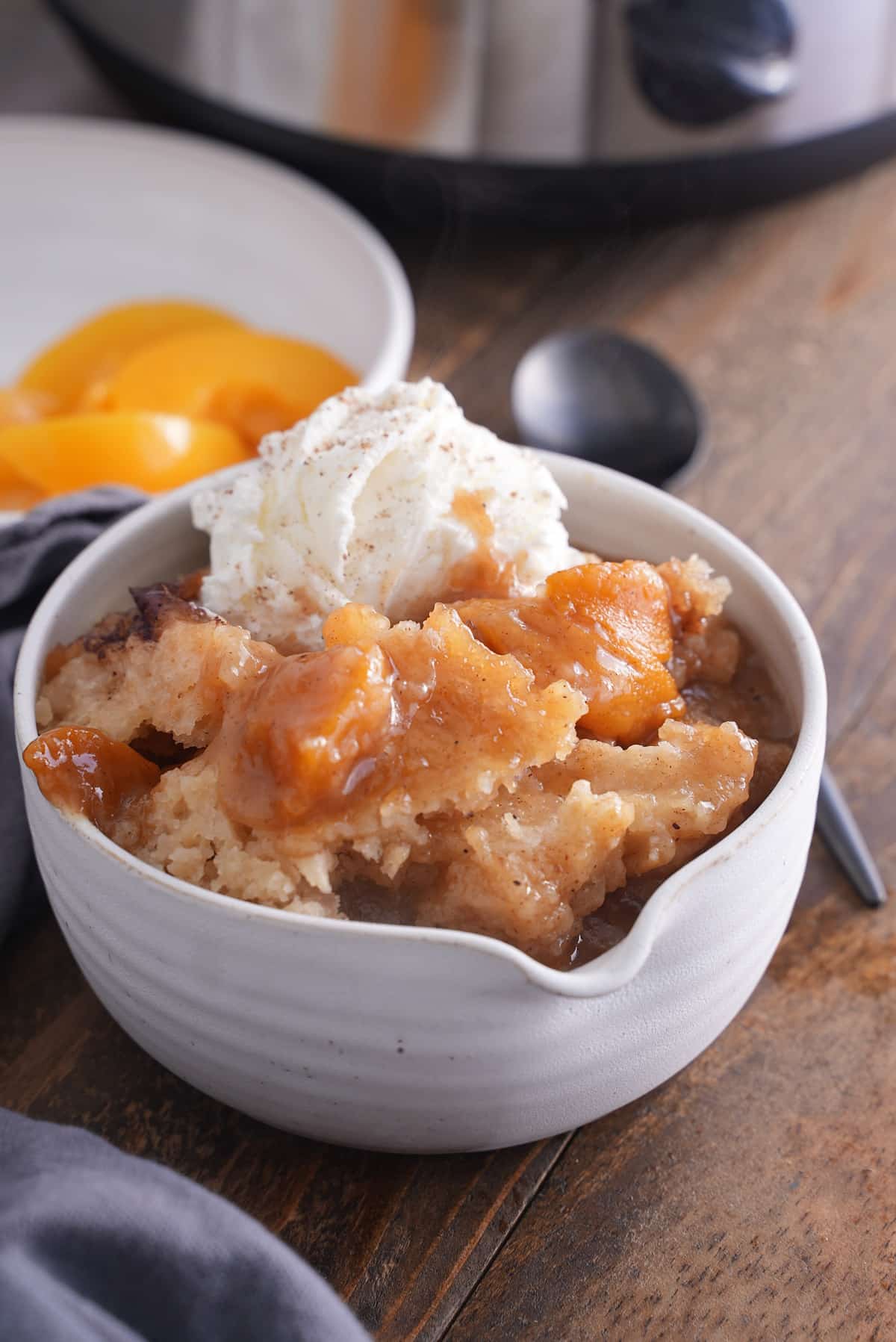 A serving of peach cobbler in a white bowl with ice cream.