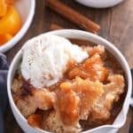 A serving of peach cobbler in a white bowl with ice cream.