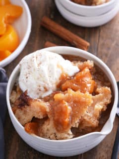 A serving of peach cobbler in a white bowl with ice cream.