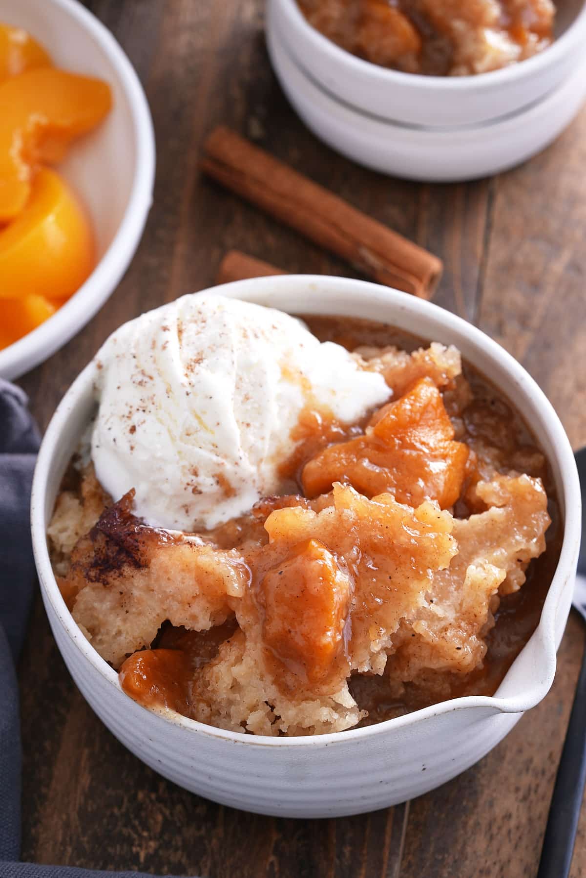 A serving of peach cobbler in a white bowl with ice cream.