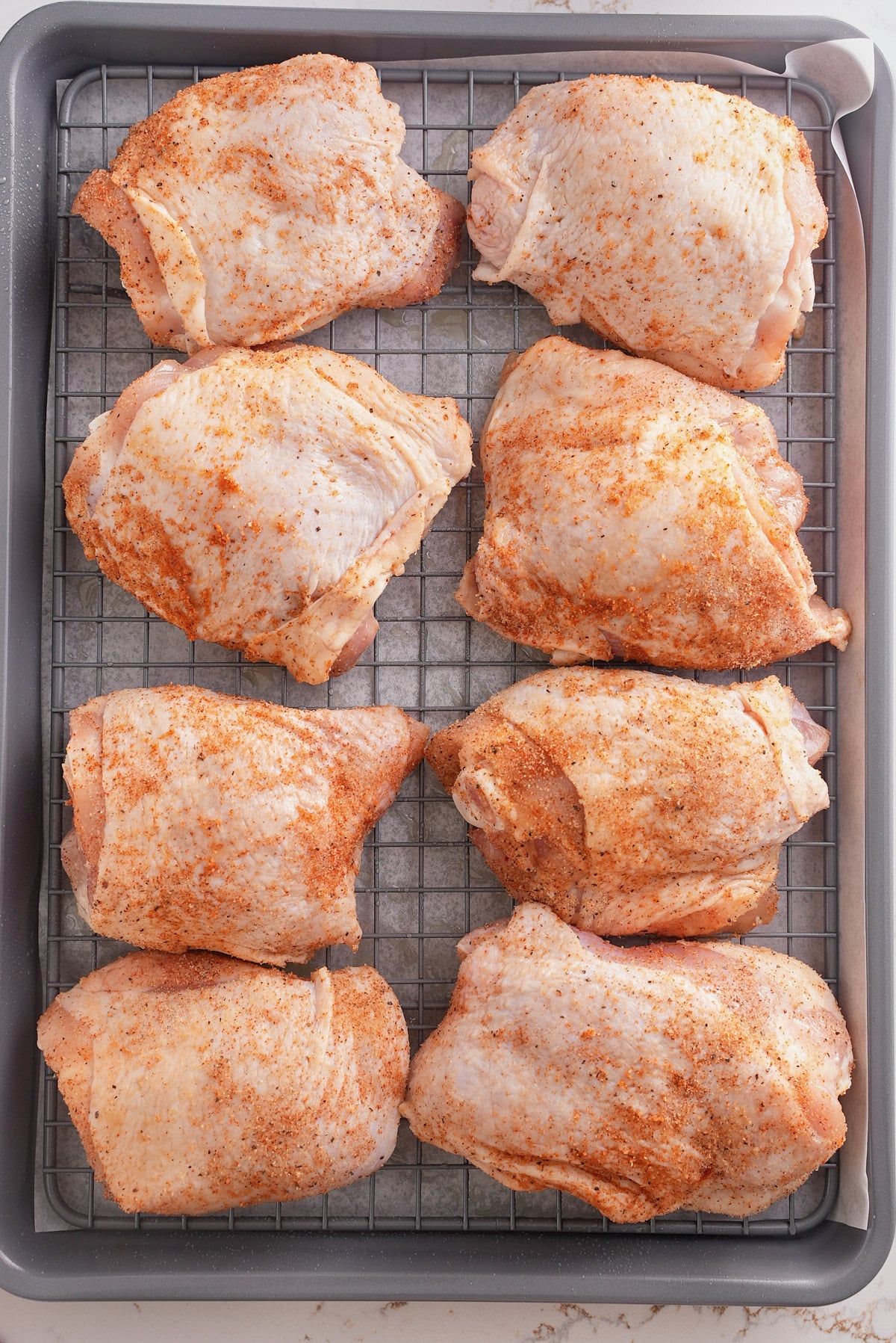 Seasoned raw chicken thighs on a baking sheet.