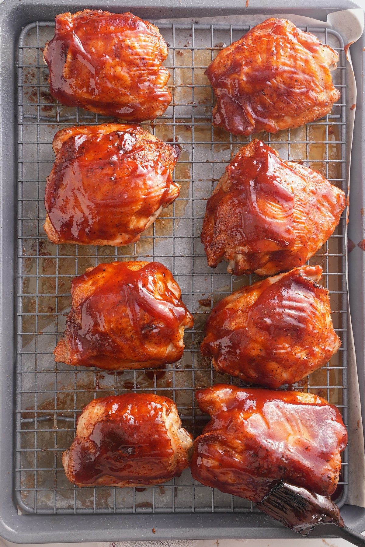 baked bbq chicken thighs on a baking sheet topped with bbq sauce.