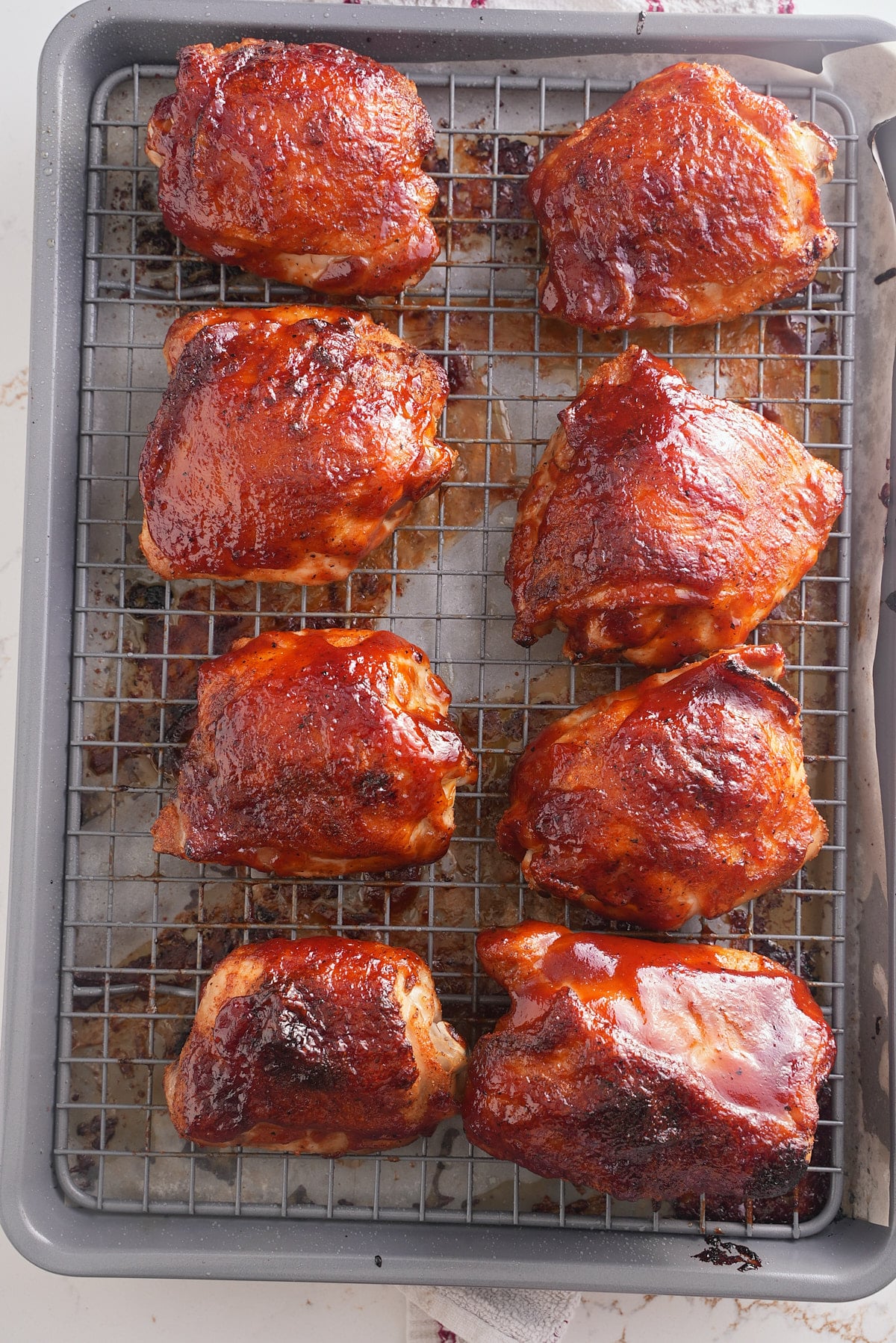 baked bbq chicken thighs on a baking sheet topped with bbq sauce.
