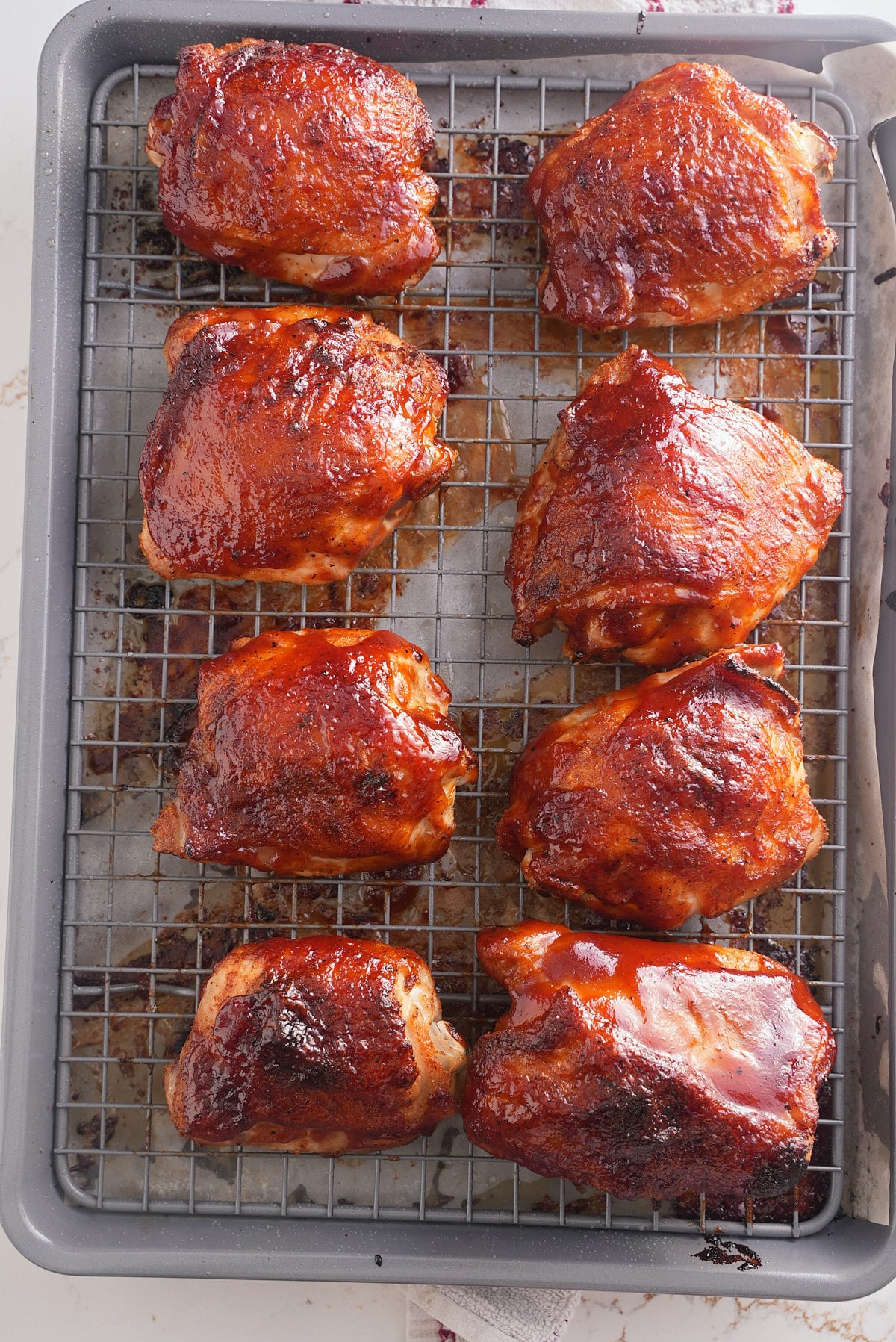 baked bbq chicken thighs on a baking sheet topped with bbq sauce.