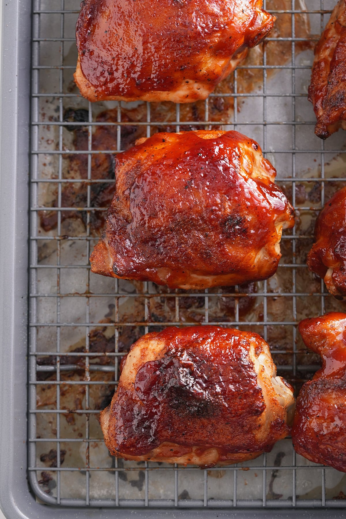 baked bbq chicken thighs on a baking sheet topped with bbq sauce.