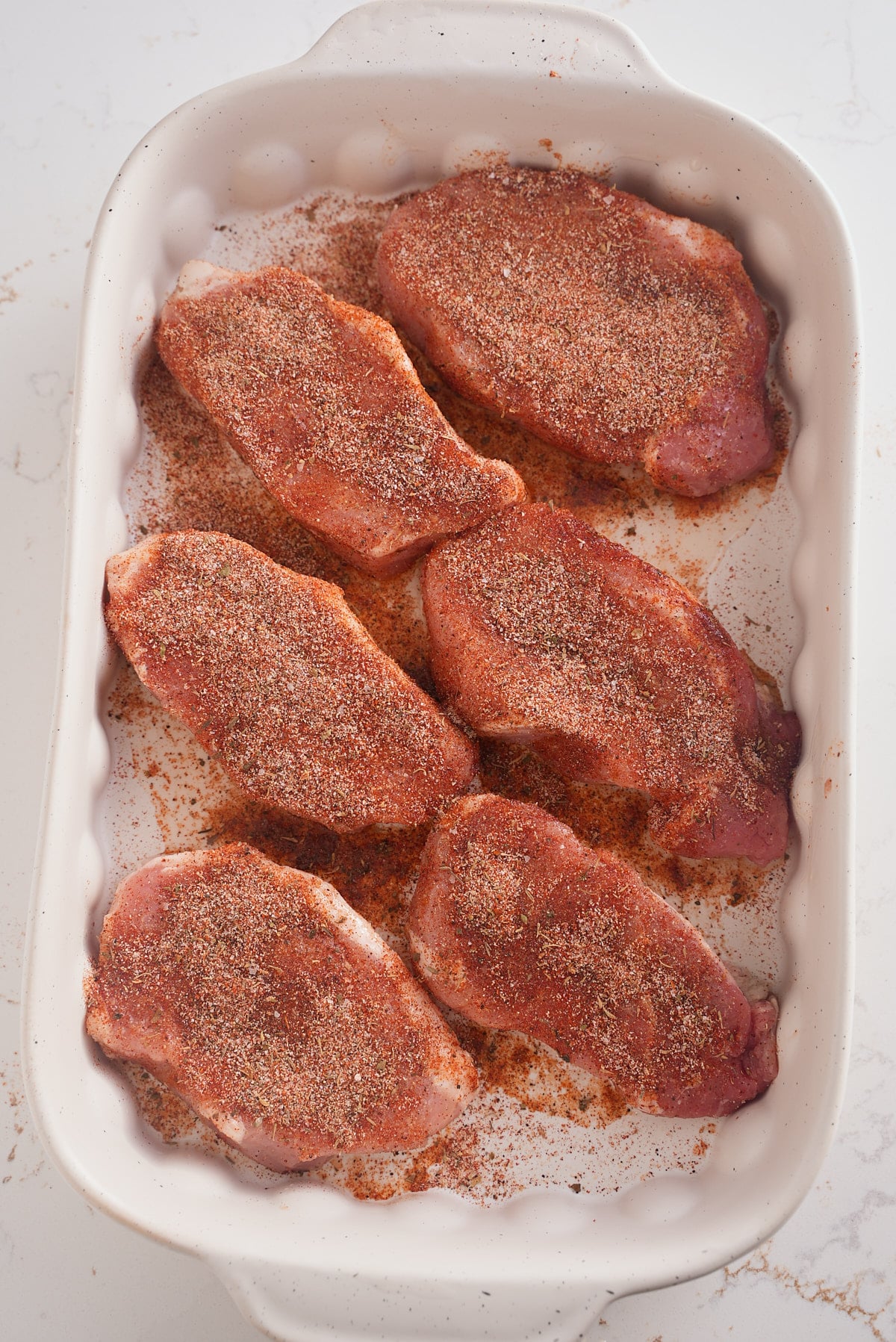 Seasoned pork chops placed in a white baking dish.
