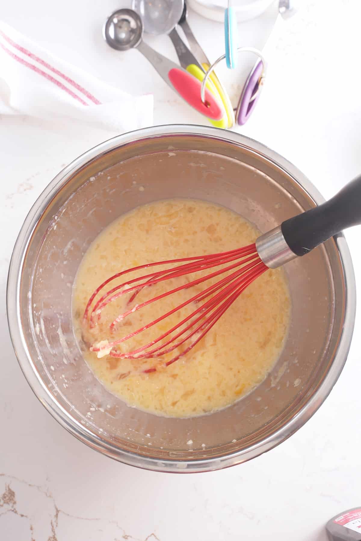 A whisk and bowl of mixed eggs, milk, melted butter and maple syrup.