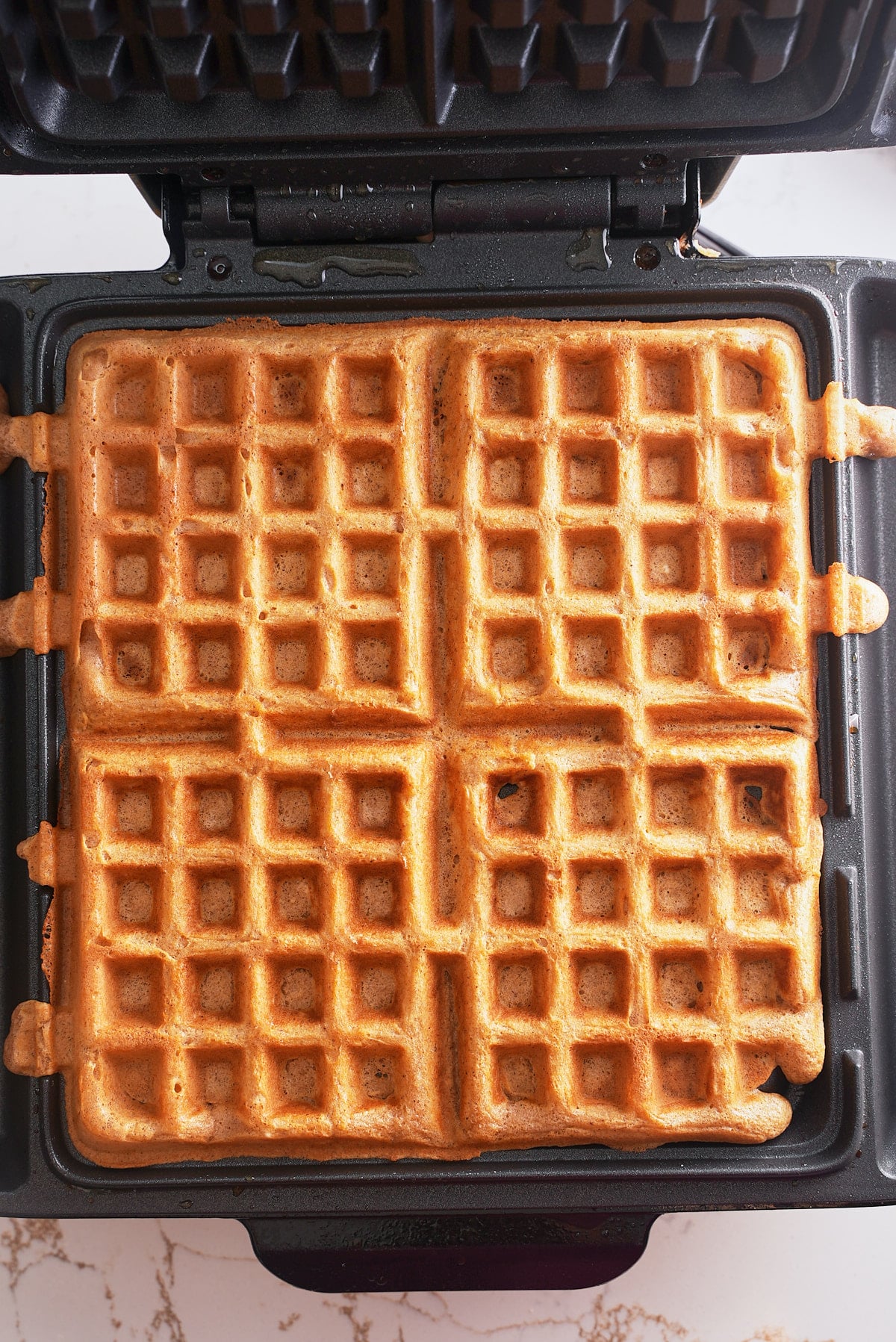 Four cooked sweet potato waffles in a waffle iron.