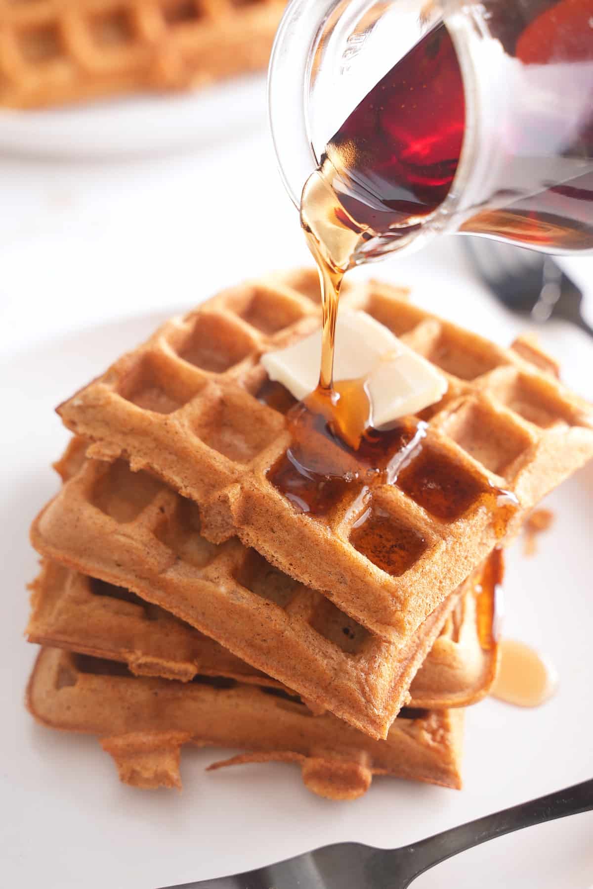 A stack of sweet potato waffles topped with butter with maple syrup being poured over.