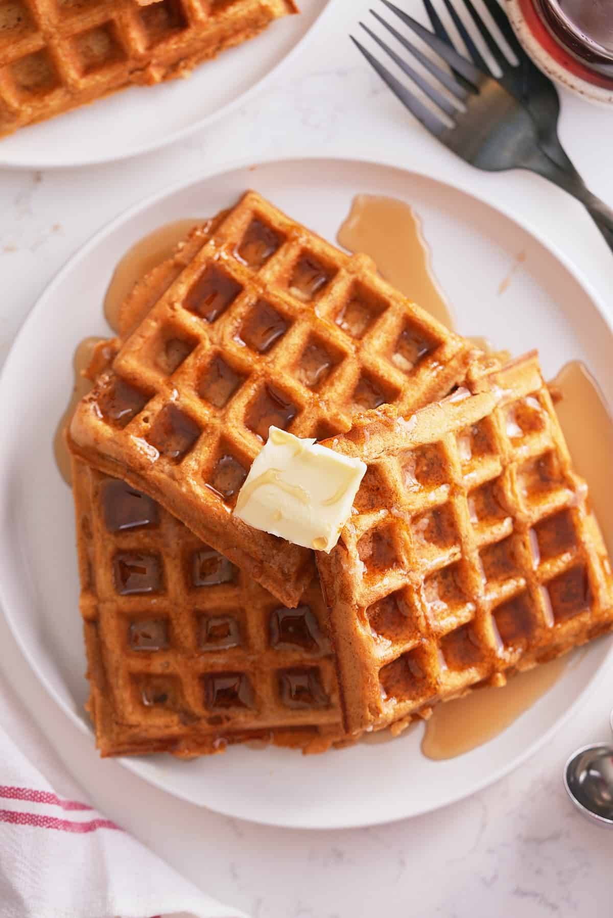 A plate of sweet potato waffles topped with butter and a drizzle of maple syrup.