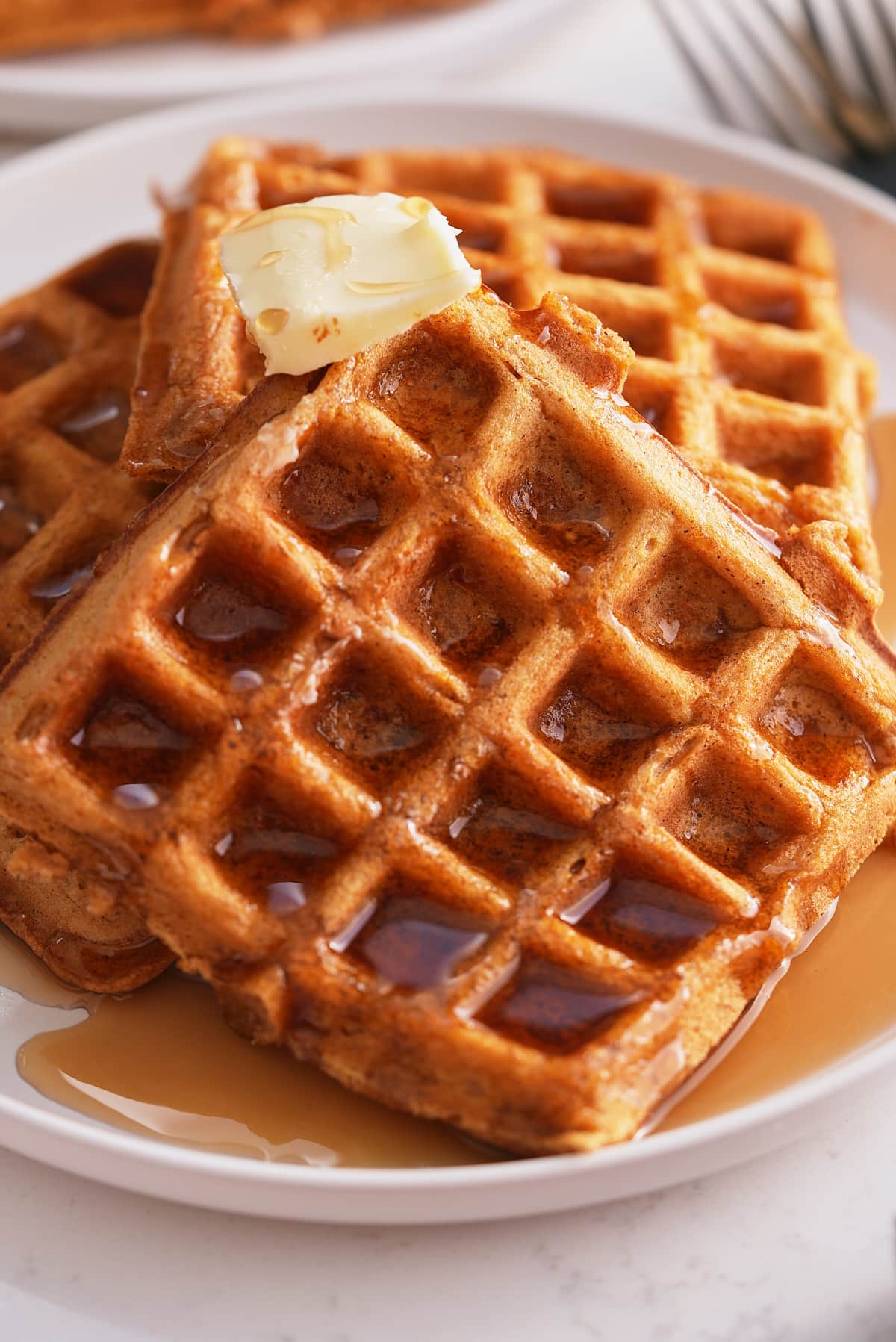 A plate of sweet potato waffles topped with butter and a drizzle of maple syrup.