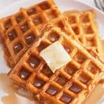 A plate of sweet potato waffles topped with butter and a drizzle of maple syrup.