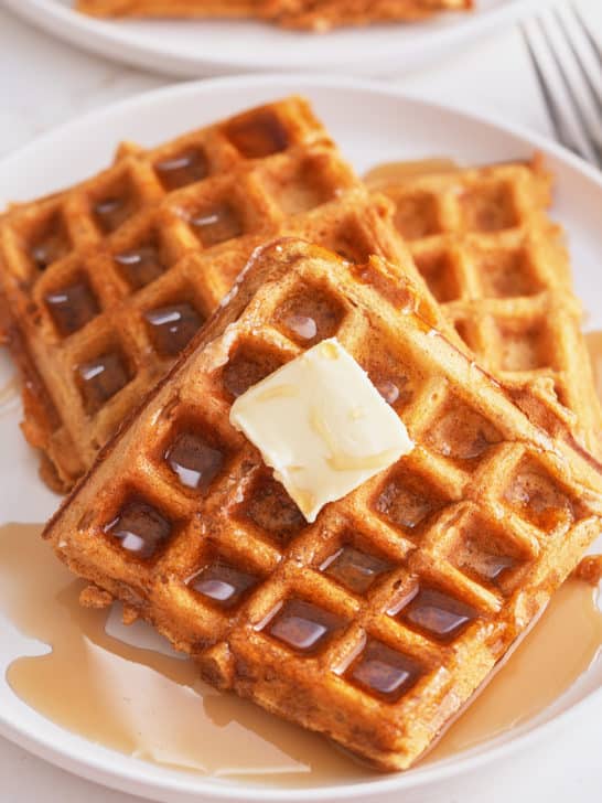 A plate of sweet potato waffles topped with butter and a drizzle of maple syrup.