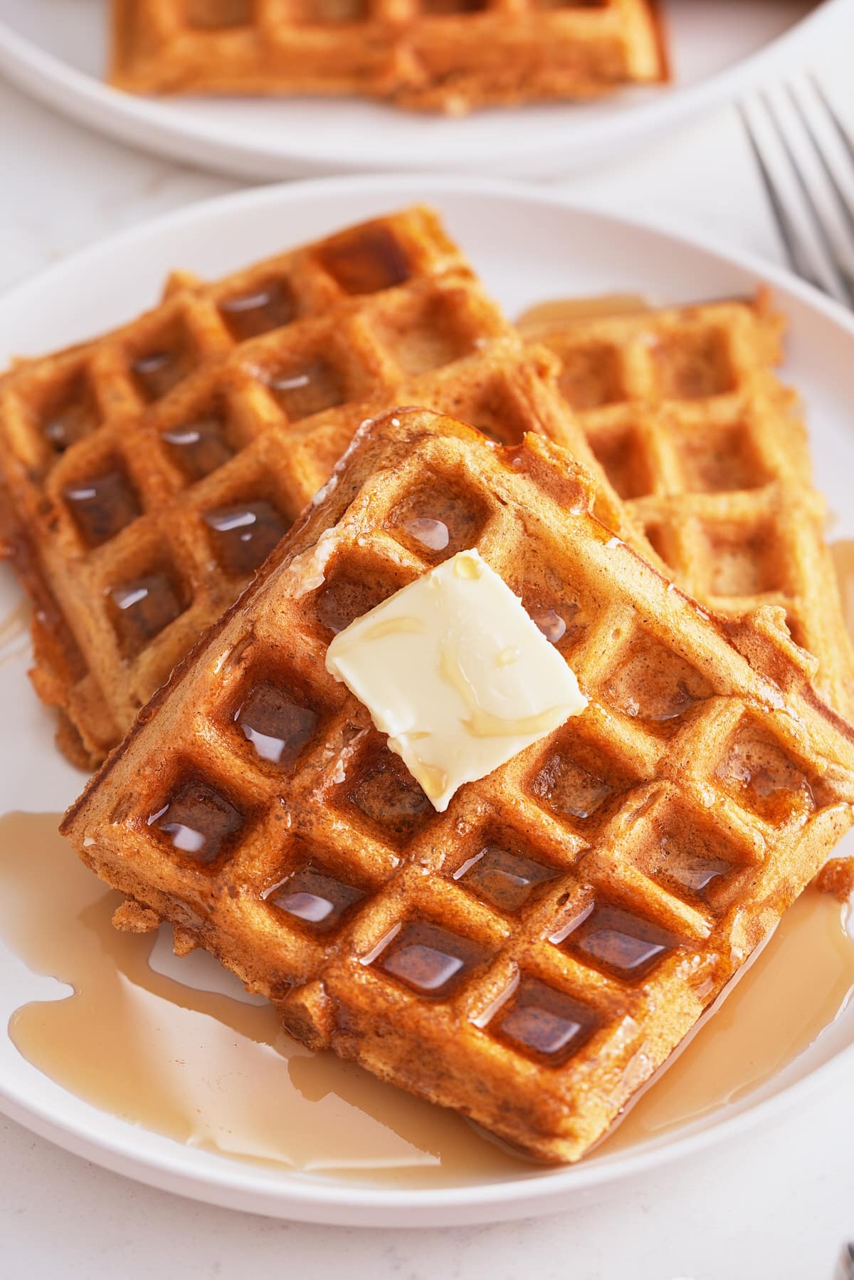 A plate of sweet potato waffles topped with butter and a drizzle of maple syrup.