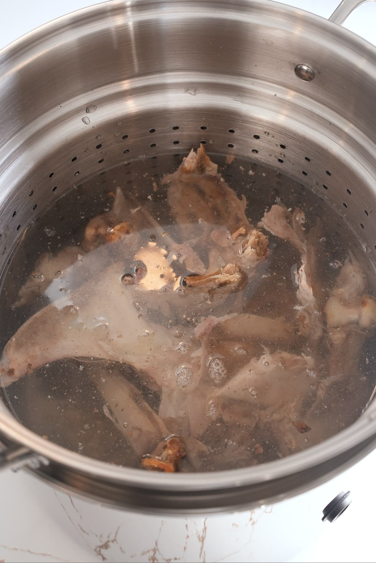 A large pot filled with turkey carcass and bones, covered in water.