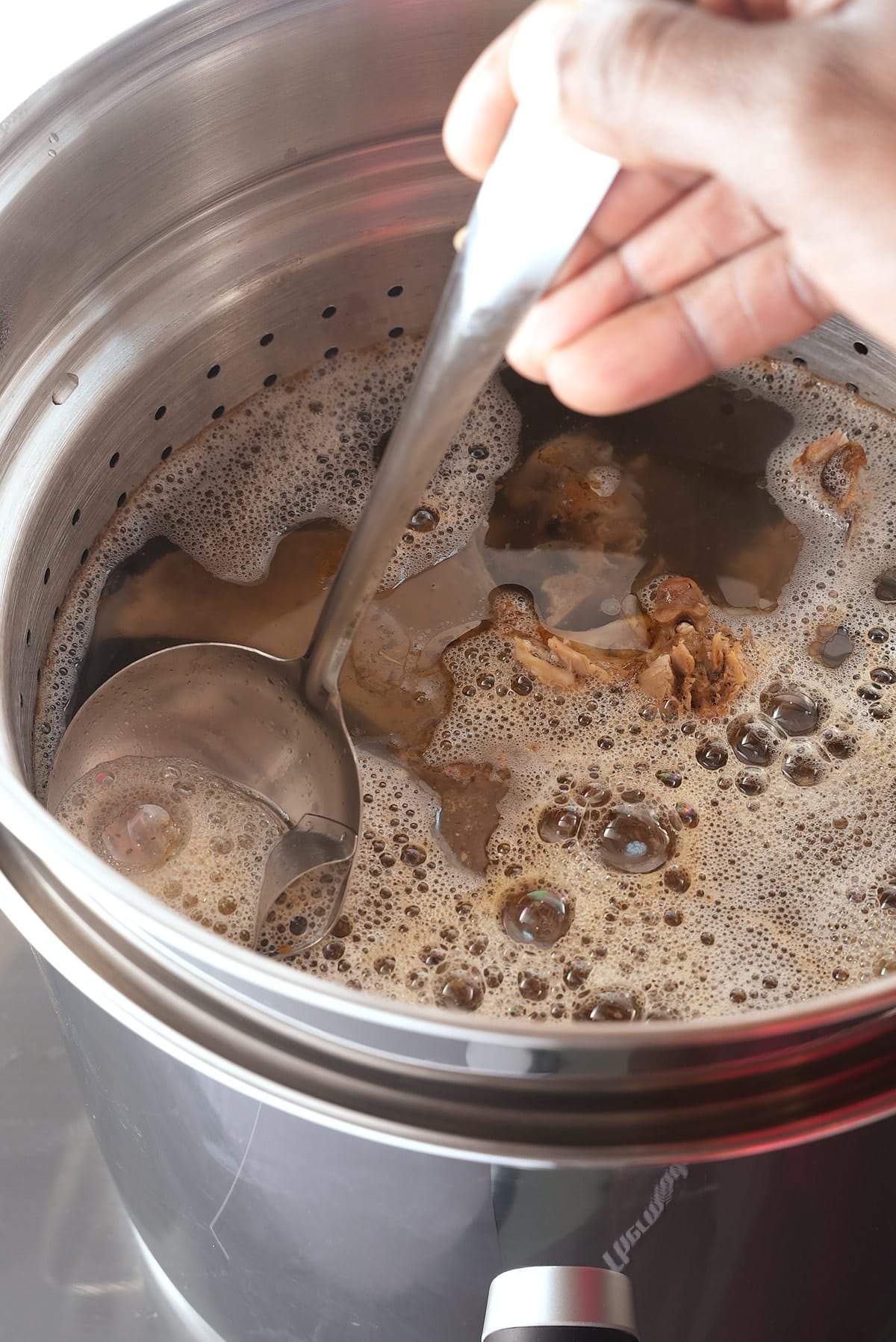 A large pot of turkey stock with the fat being spooned off.