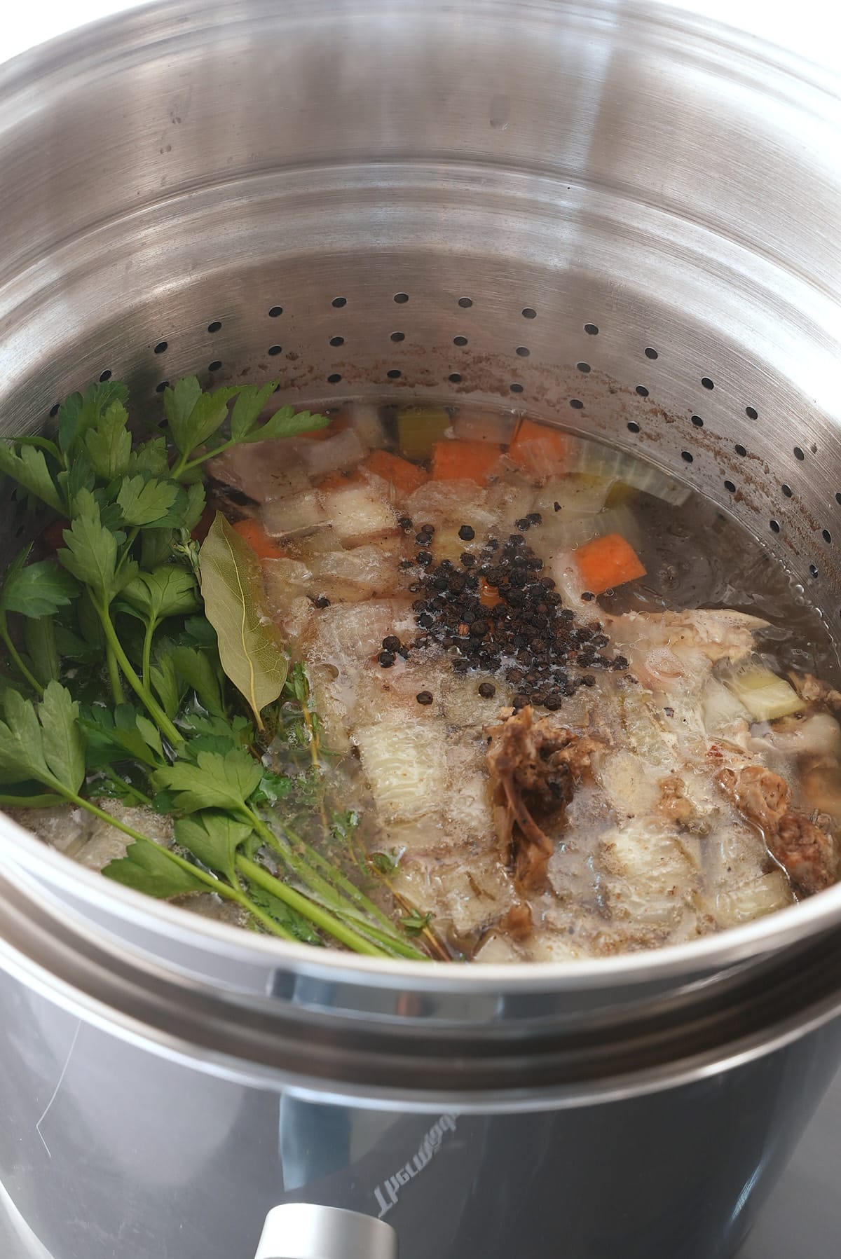 A large pot of turkey stock with added vegetables, fresh herbs and whole spices.