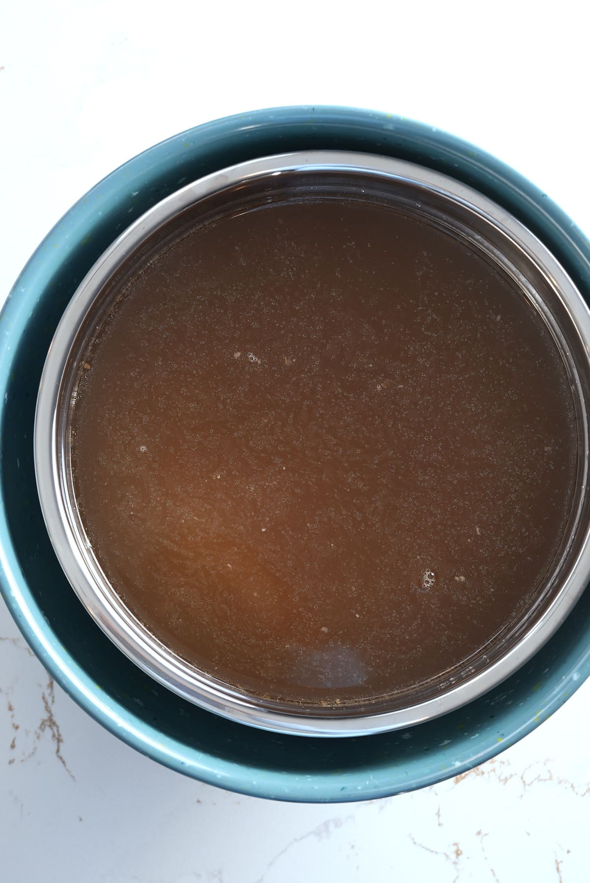 A pot of turkey stock being set inside a bowl of ice cubes to cool.