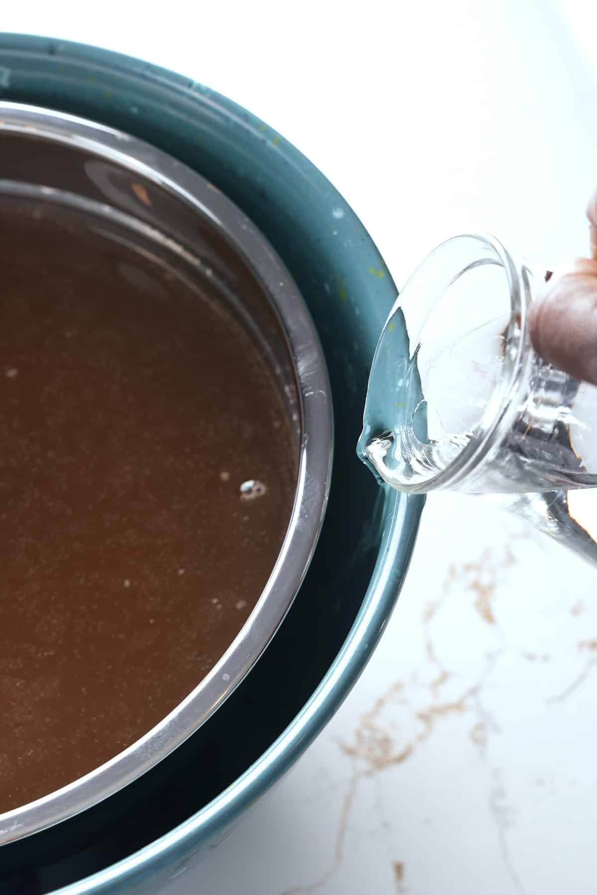 A pot of turkey stock being set inside a bowl of ice cubes to cool, with a jug of ice cold water being poured down between the 2 bowls.