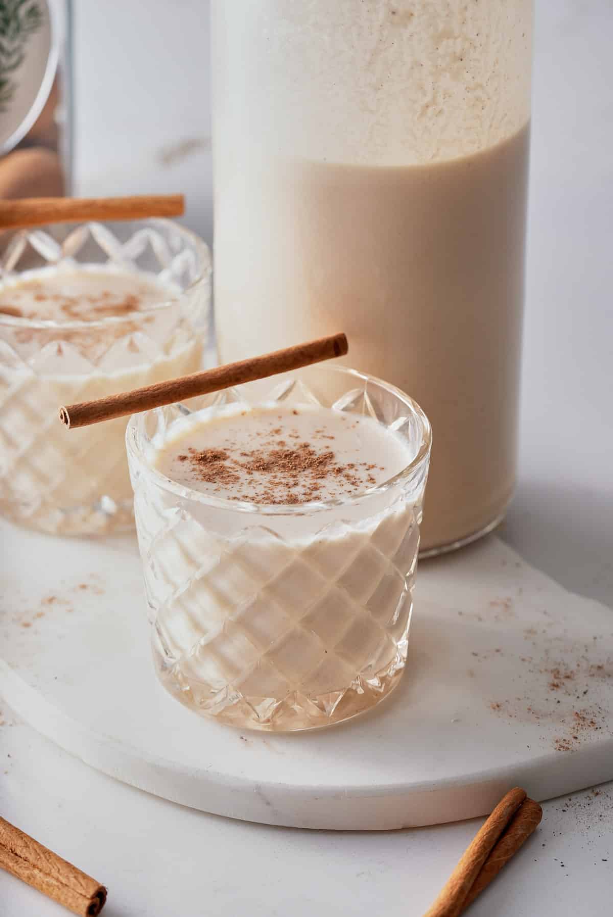 two coquito cocktails being served with a cinnamon stick on top.