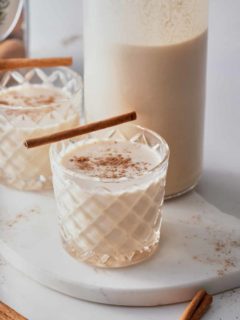 two coquito cocktails being served with a cinnamon stick on top.