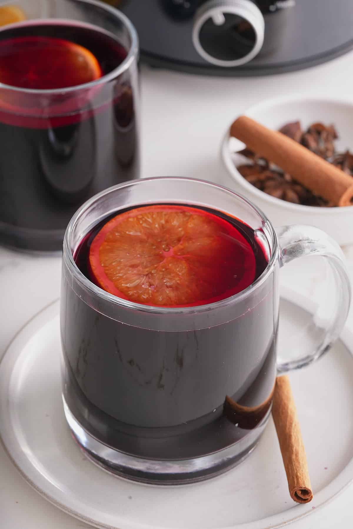 Two glass cups filled with mulled wine and topped with a slice of mulled orange with whole spices set alongside.