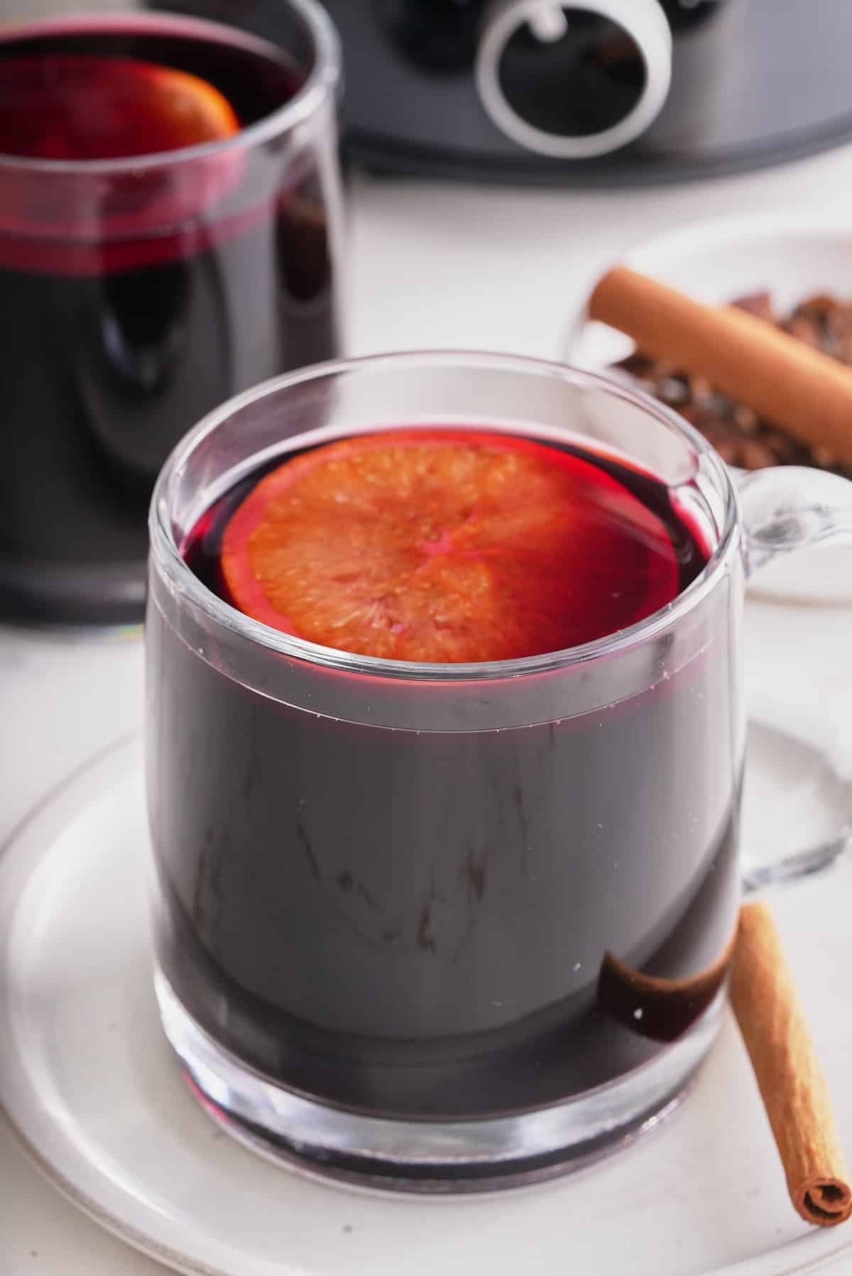 Two glass cups filled with mulled wine and topped with a slice of mulled orange with whole spices set alongside.