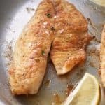 close up of Pan fried fish in a large skillet with added slices of fresh lemon.