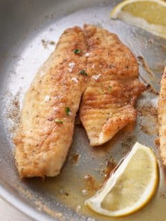 close up of Pan fried fish in a large skillet with added slices of fresh lemon.