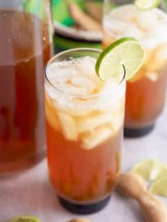 Two glasses of iced tamarind juice garnished with a slice of fresh lime.