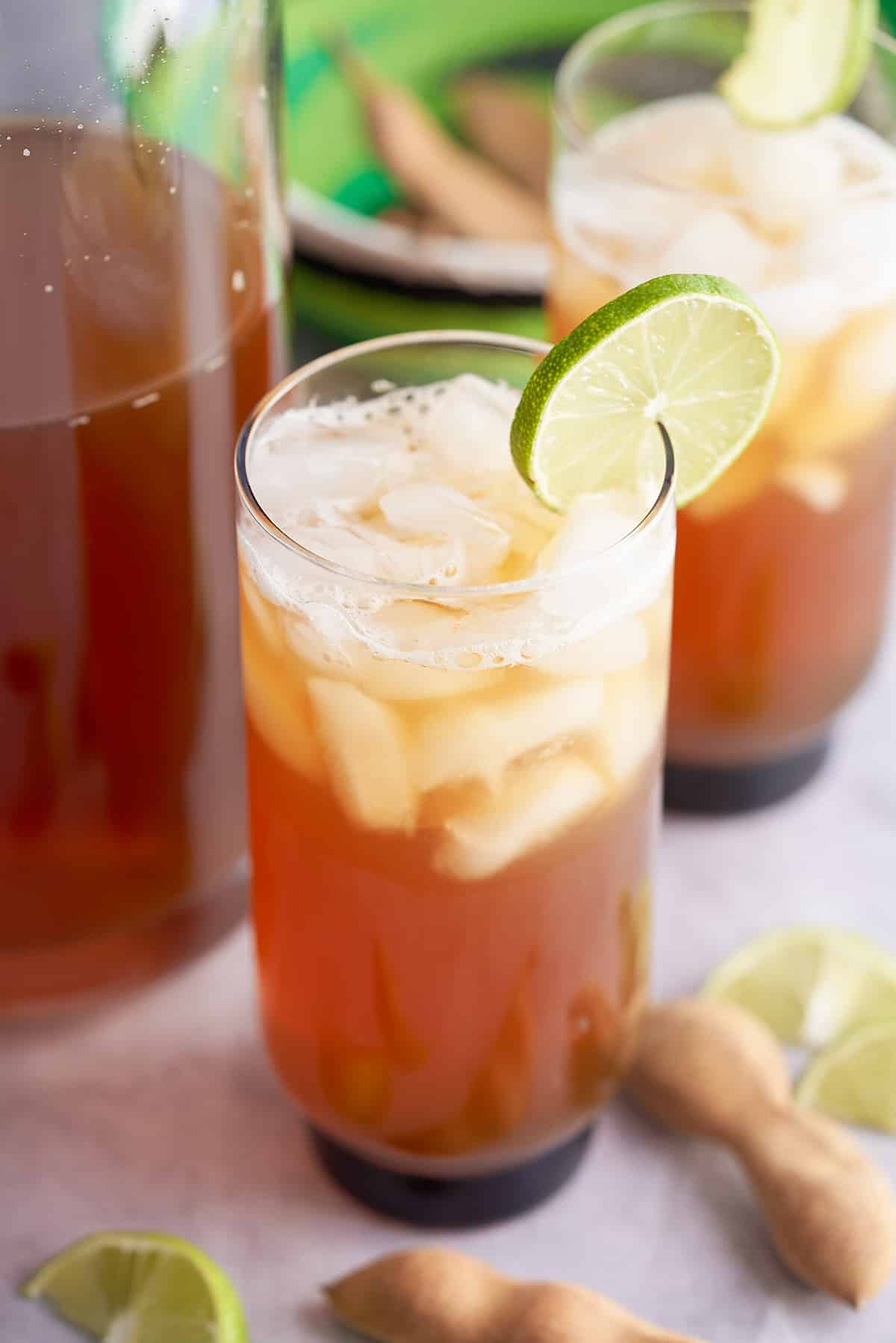 Two glasses of iced tamarind juice garnished with a slice of fresh lime.