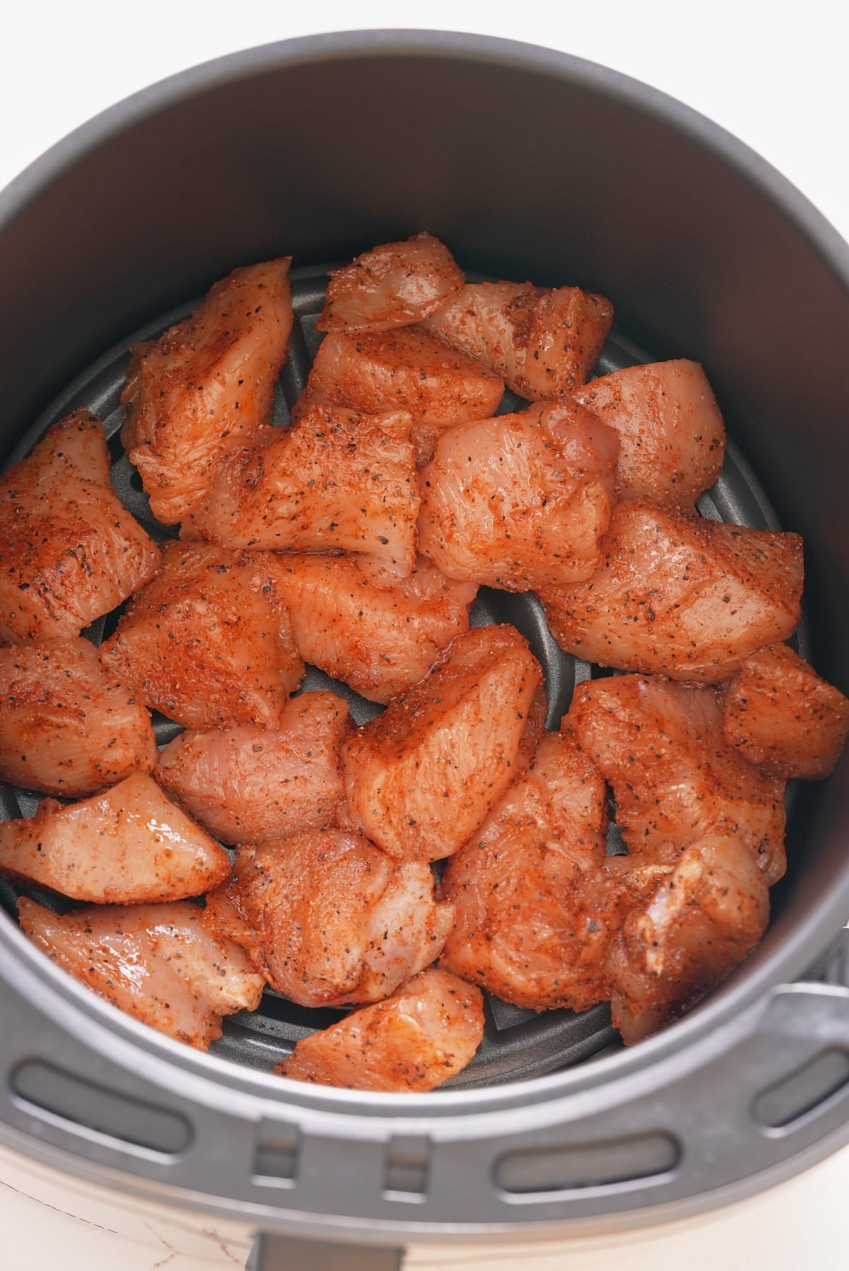 Spiced and seasoned chunks of chicken breast laid in a single layer in an air fryer basket.