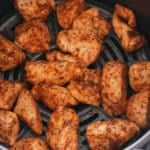 Cooked chicken chunks in an air fryer basket.