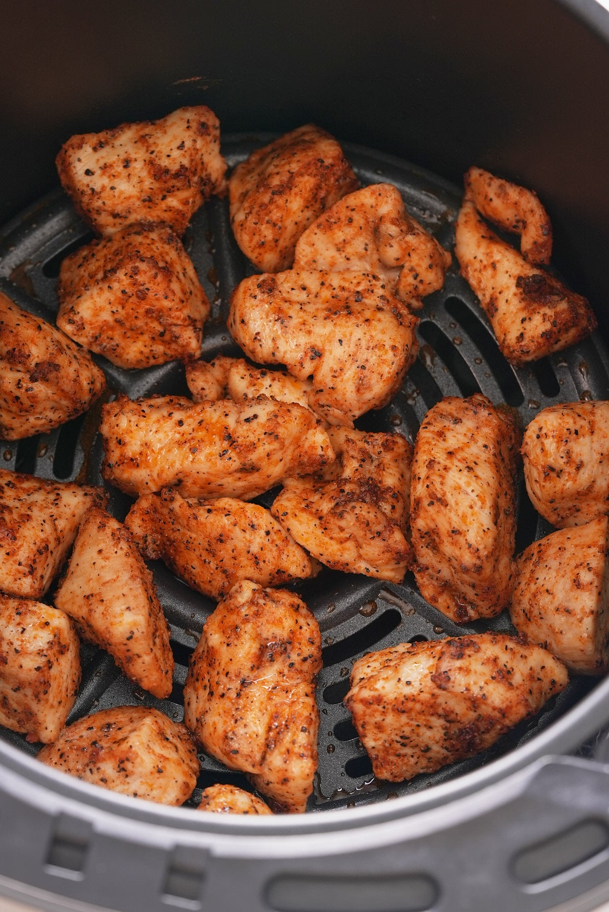 Cooked chicken chunks in an air fryer basket.