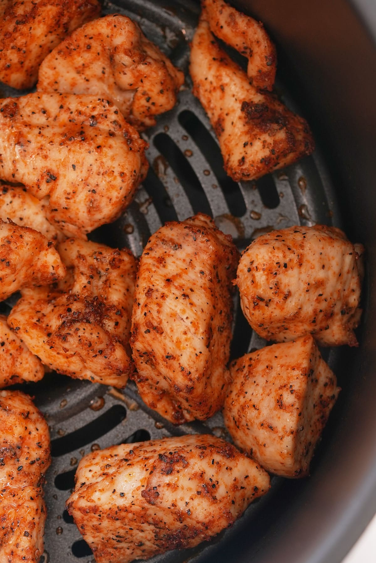 Close up of cooked chicken chunks in an air fryer basket.