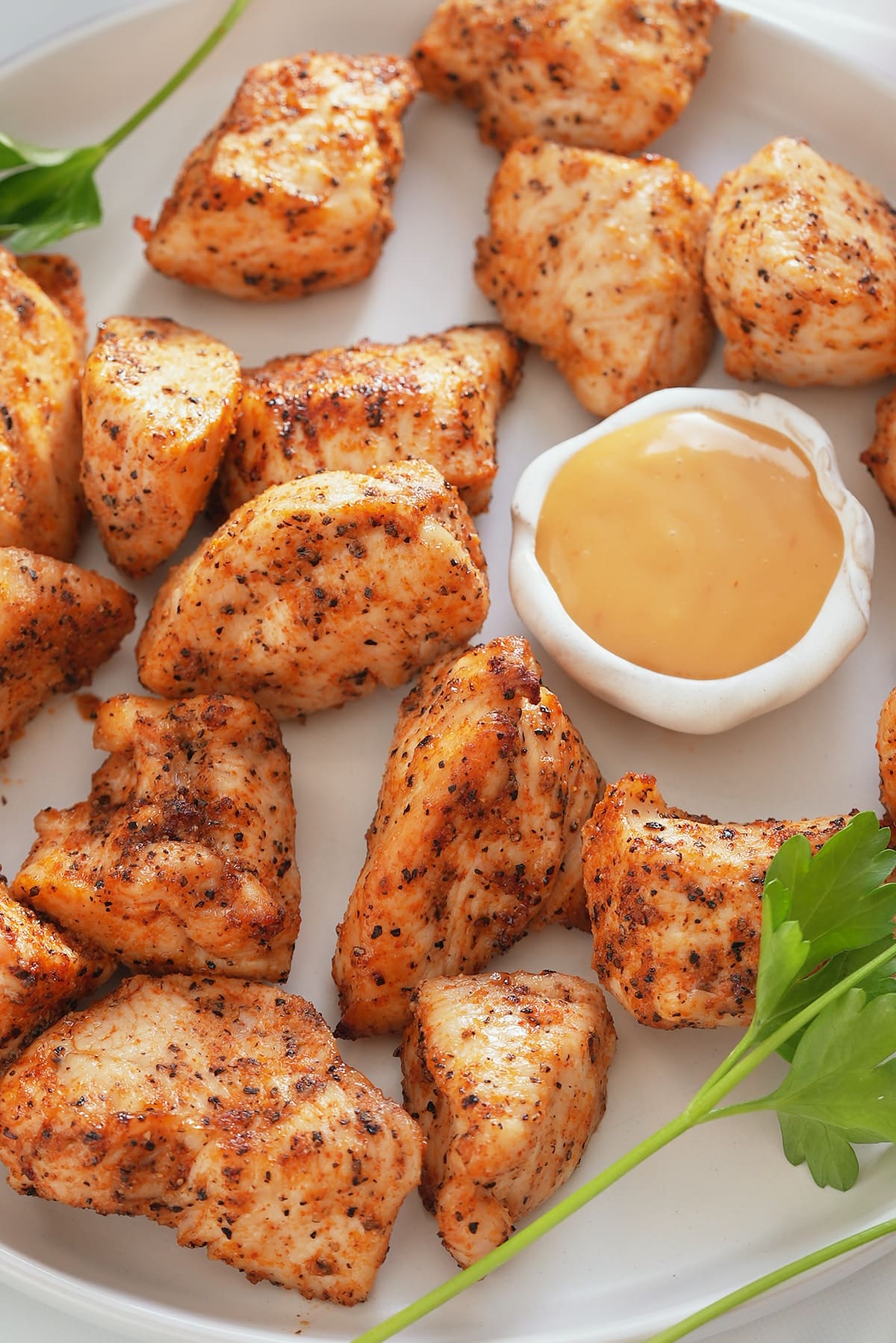 Air fryer chicken bites set on a white serving plate with a bowl of dipping sauce set alongside.