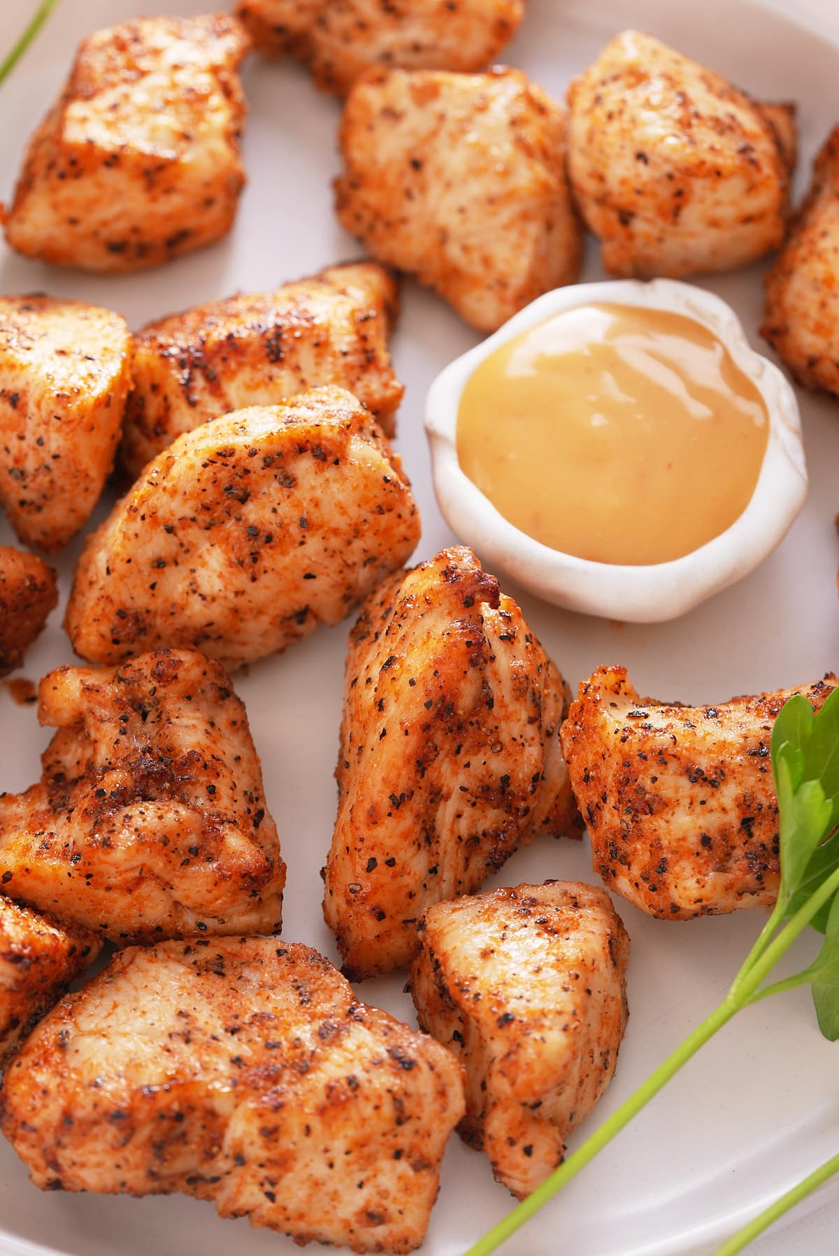 Air fryer chicken bites set on a white serving plate with a bowl of dipping sauce set alongside.