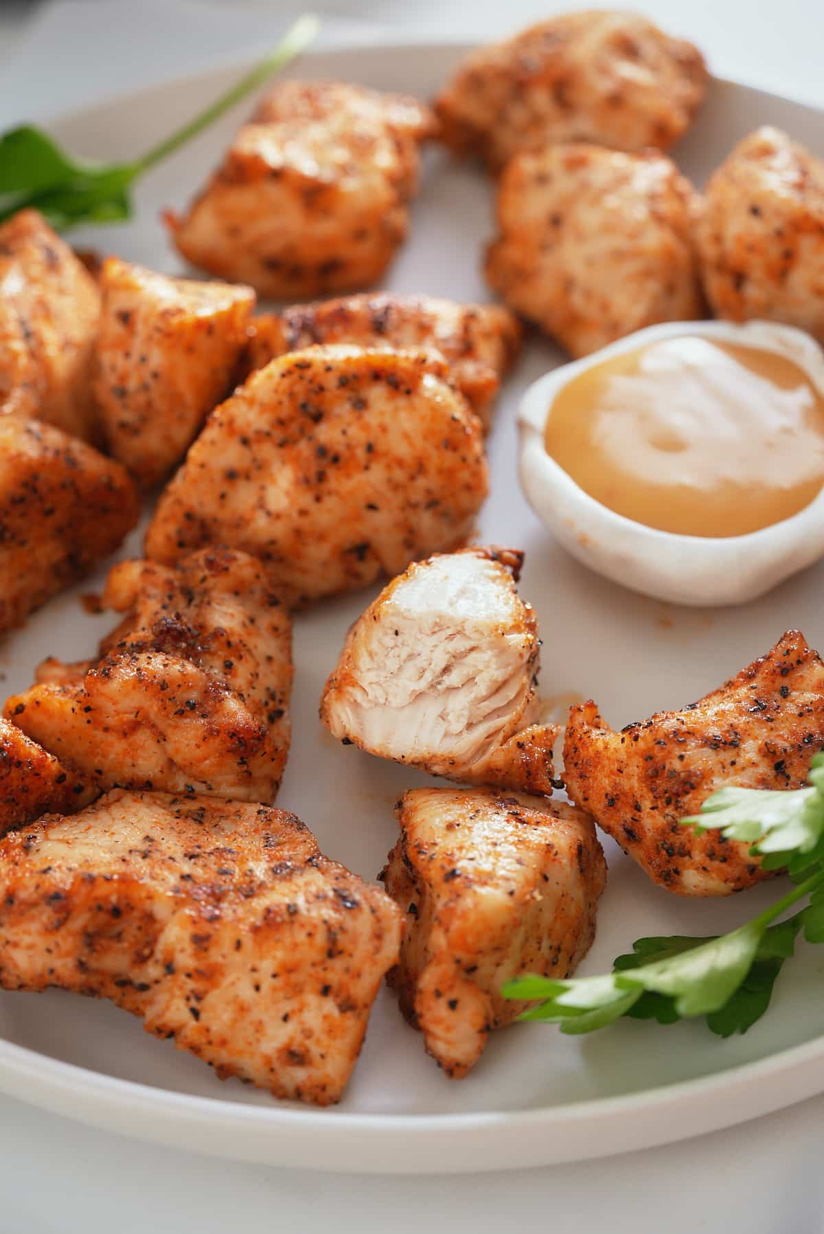 Air fryer chicken bites set on a white serving plate with a bowl of dipping sauce set alongside.