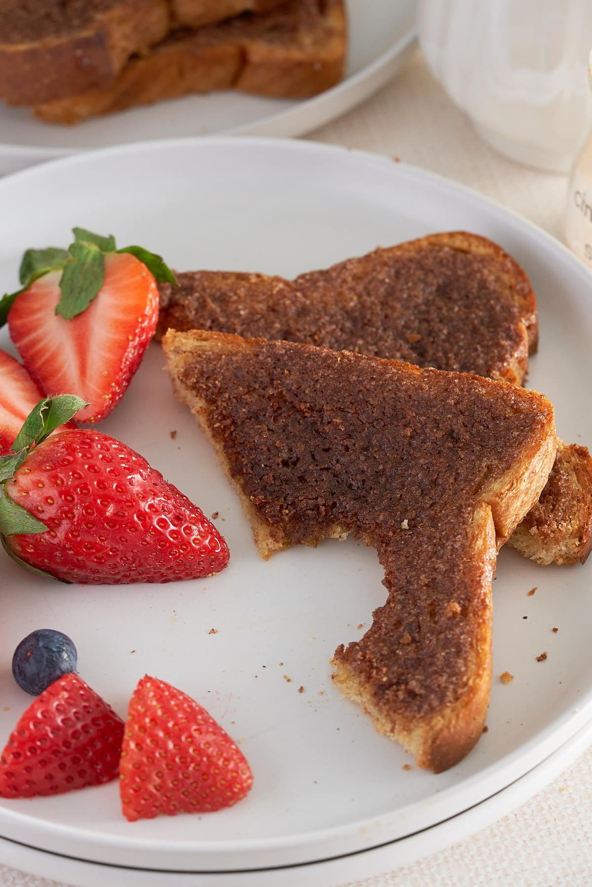 A white plate of sliced cinnamon toast with sliced strawberries.