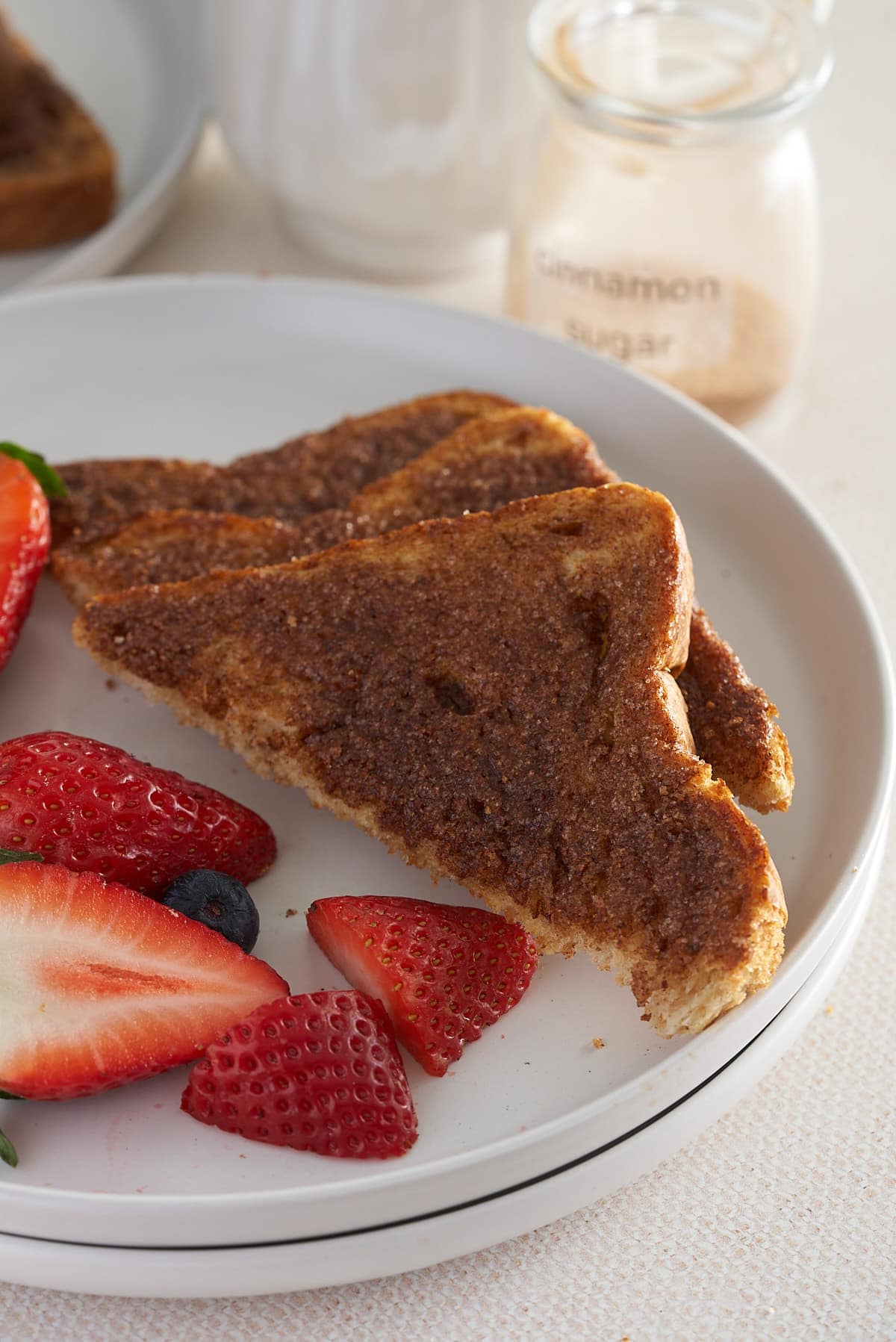 A white plate of sliced cinnamon toast with sliced strawberries.
