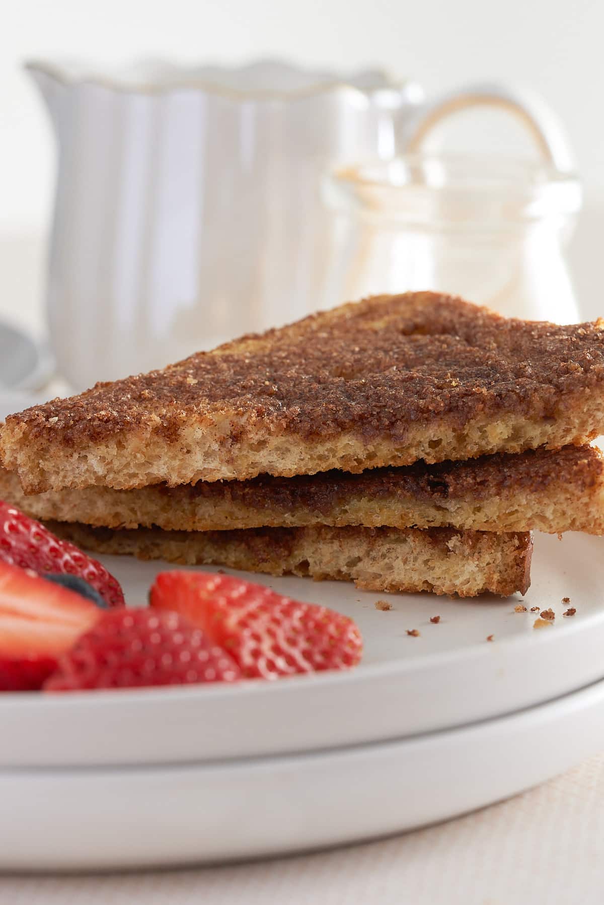 A white plate of sliced cinnamon toast with sliced strawberries.