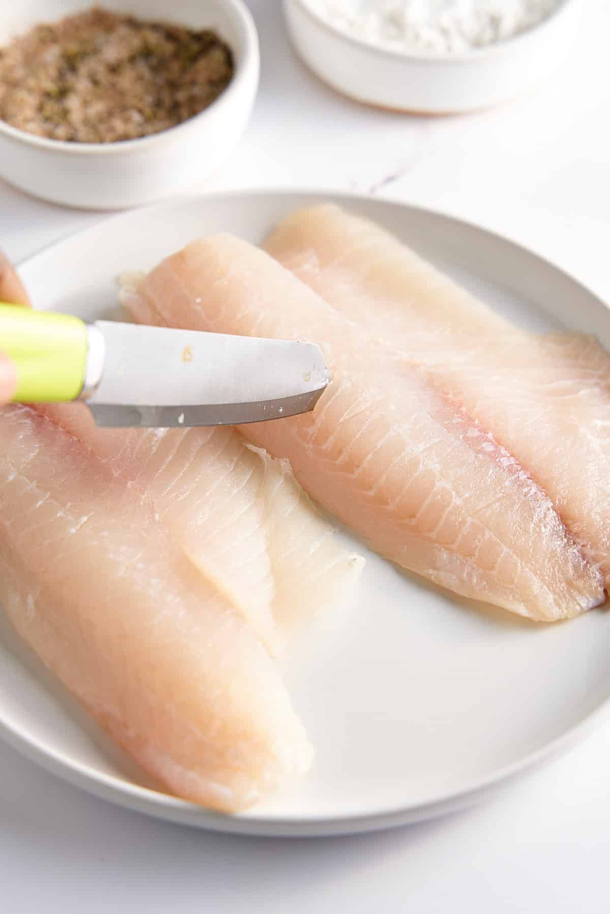 2 white fish filets being scored with a knife.