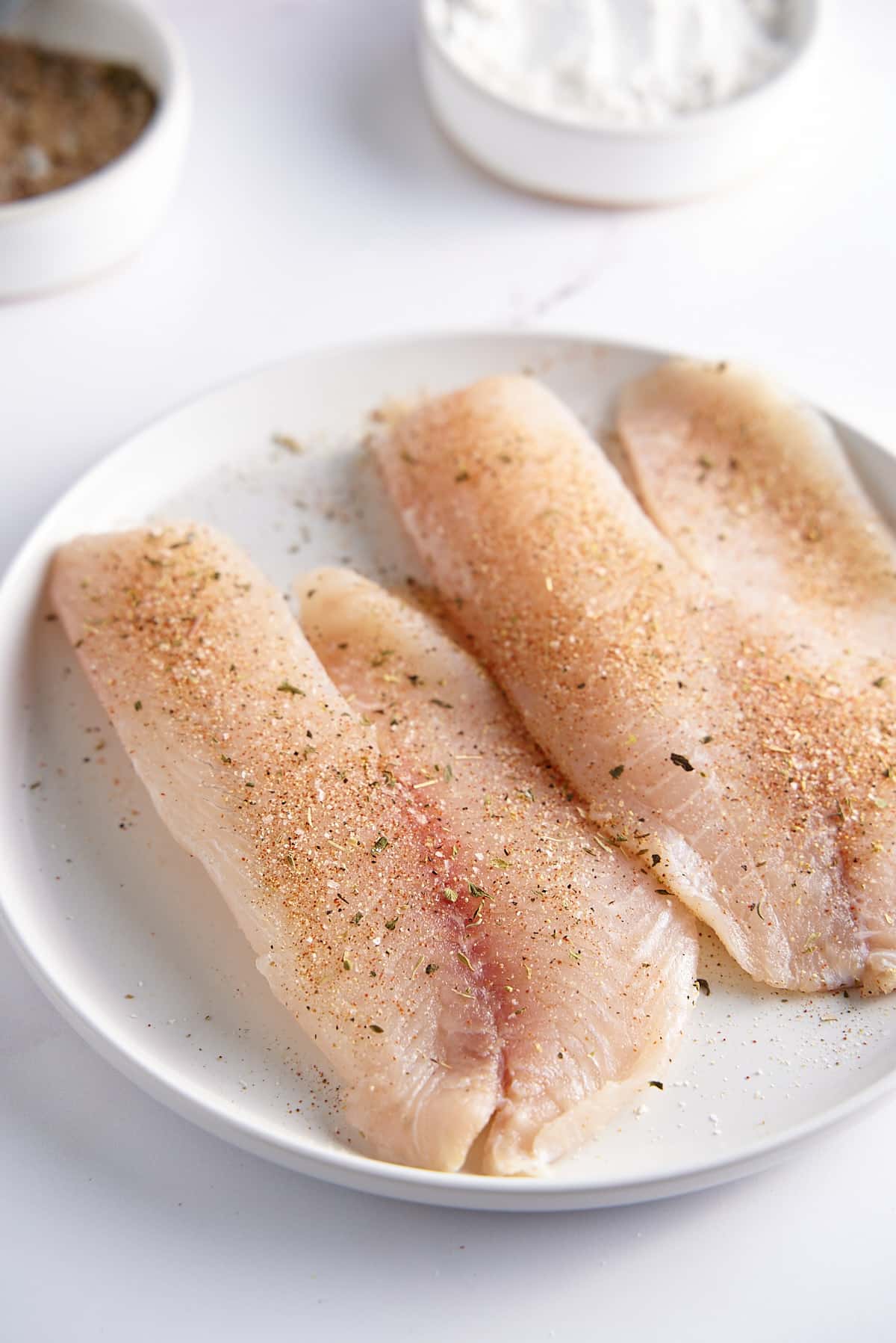 A plate with 2 seasoned white fish filets.