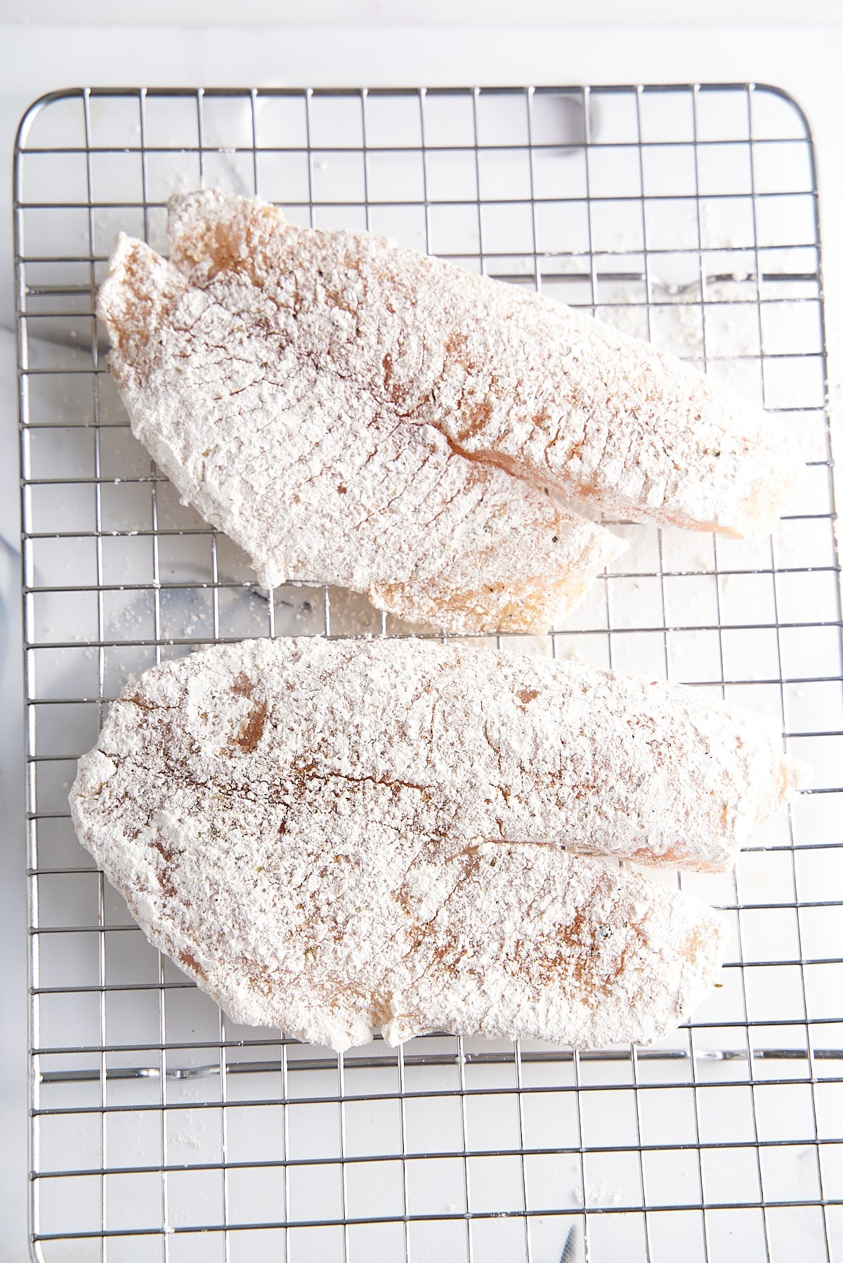 2 white fish filets coated in flour and resting on a wire rack.