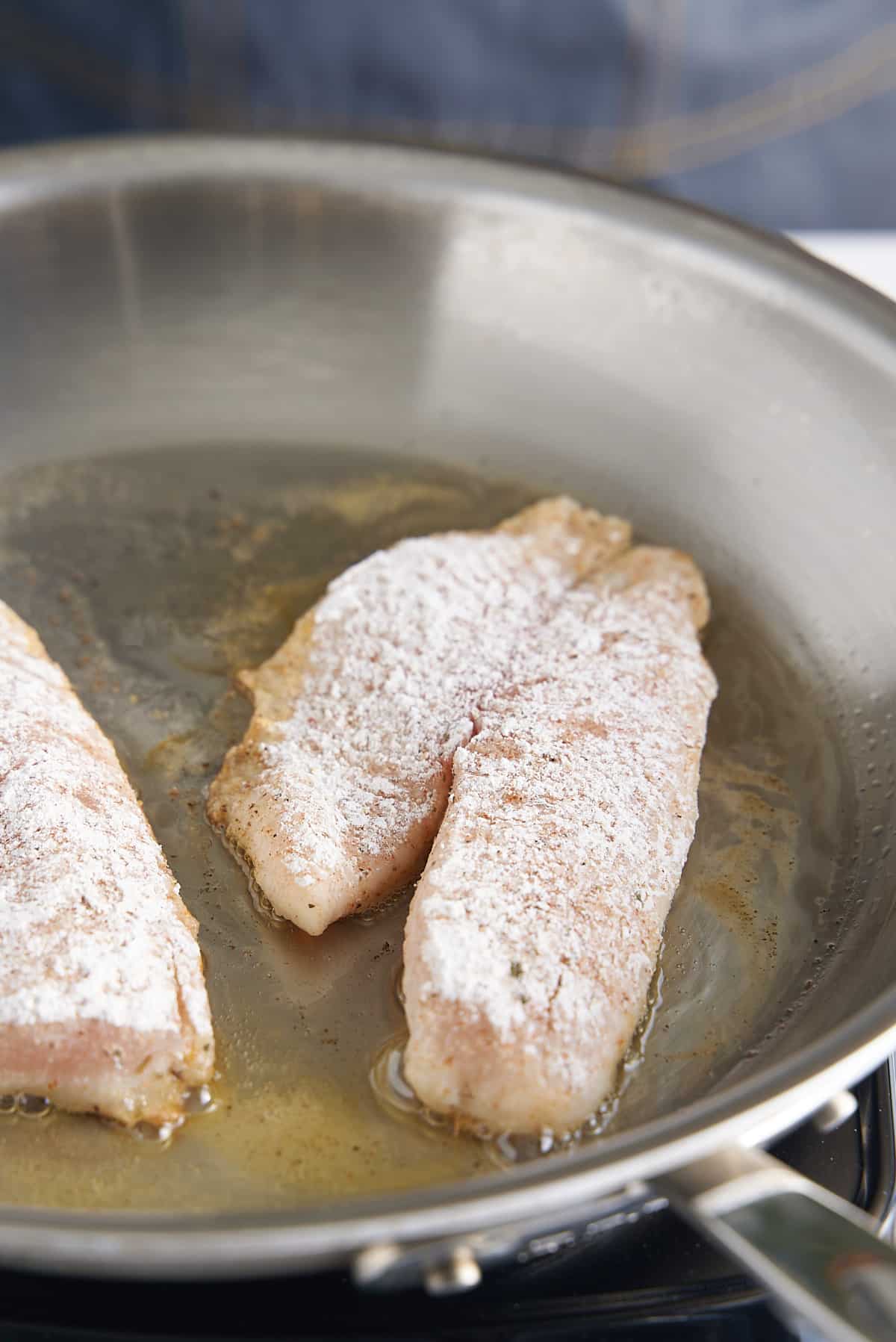 2 white fish filets sauteeing in a large skillet.
