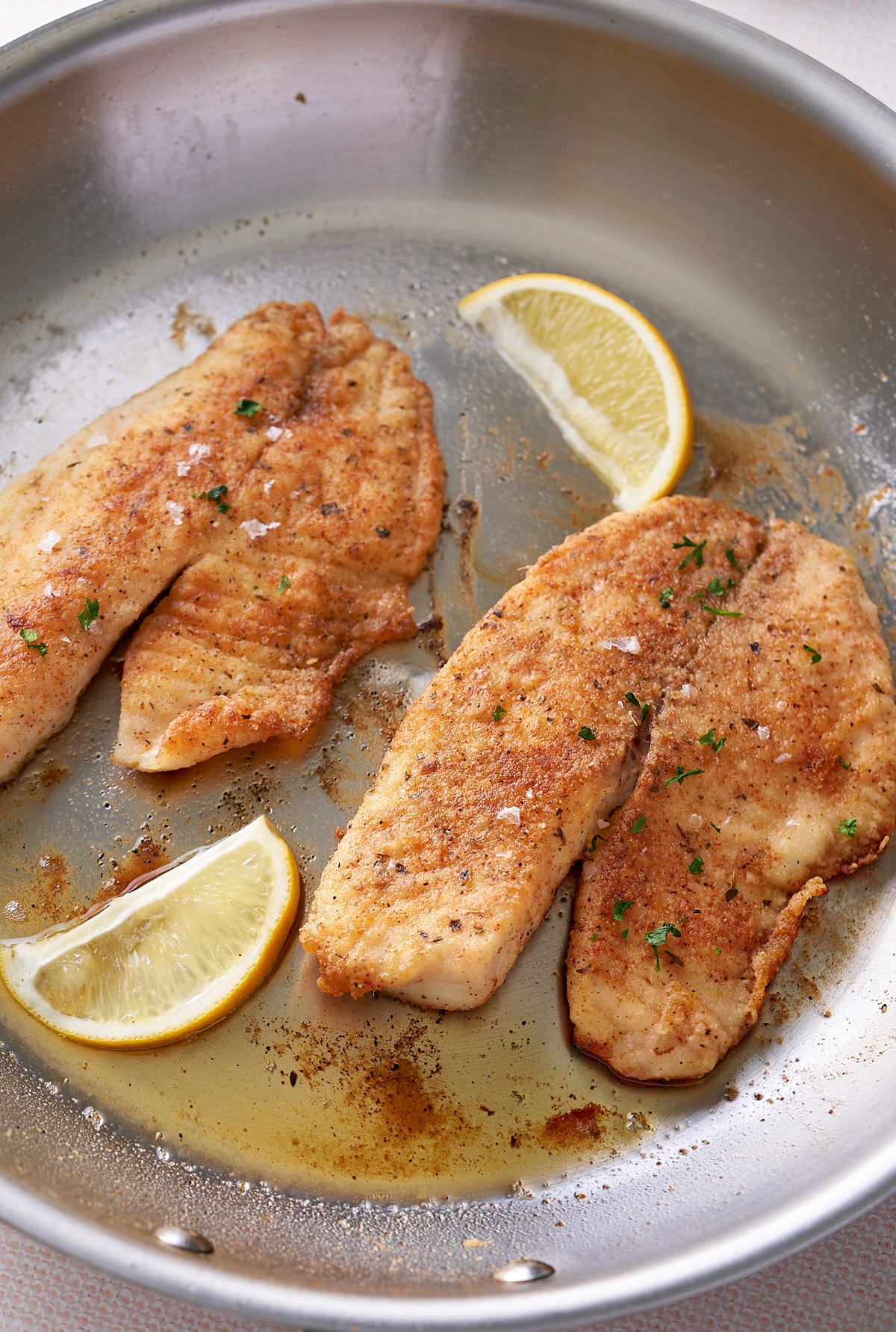 2 sauteed white fish filets in a large skillet with added slices of fresh lemon.